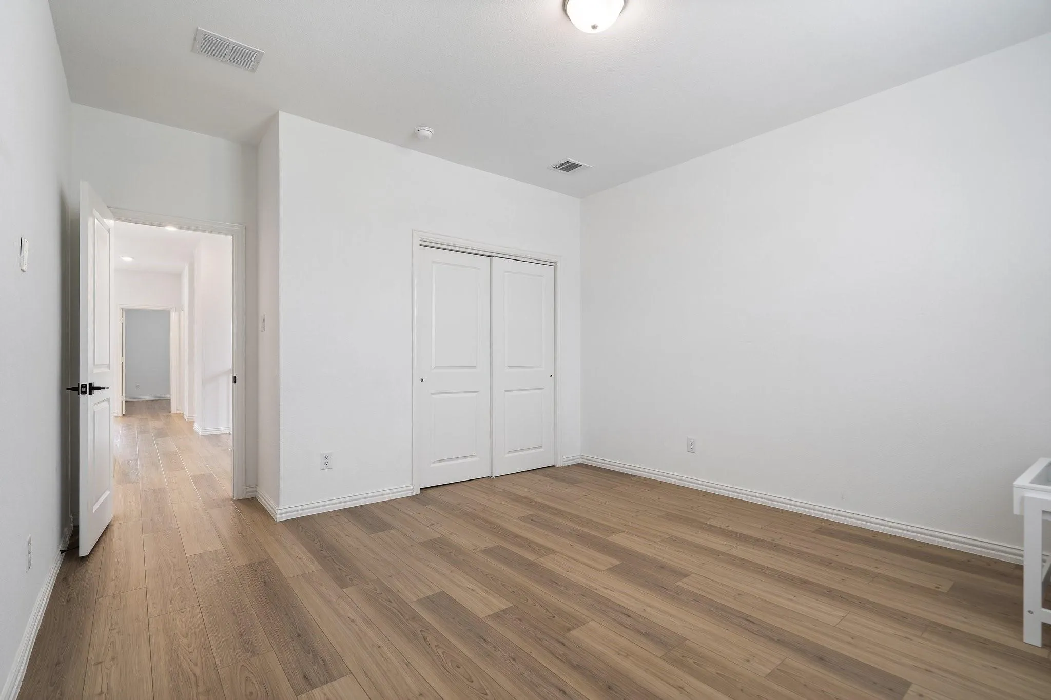 Bright interior room featuring wood-finish flooring, white walls, and a ceiling-mounted light fixture