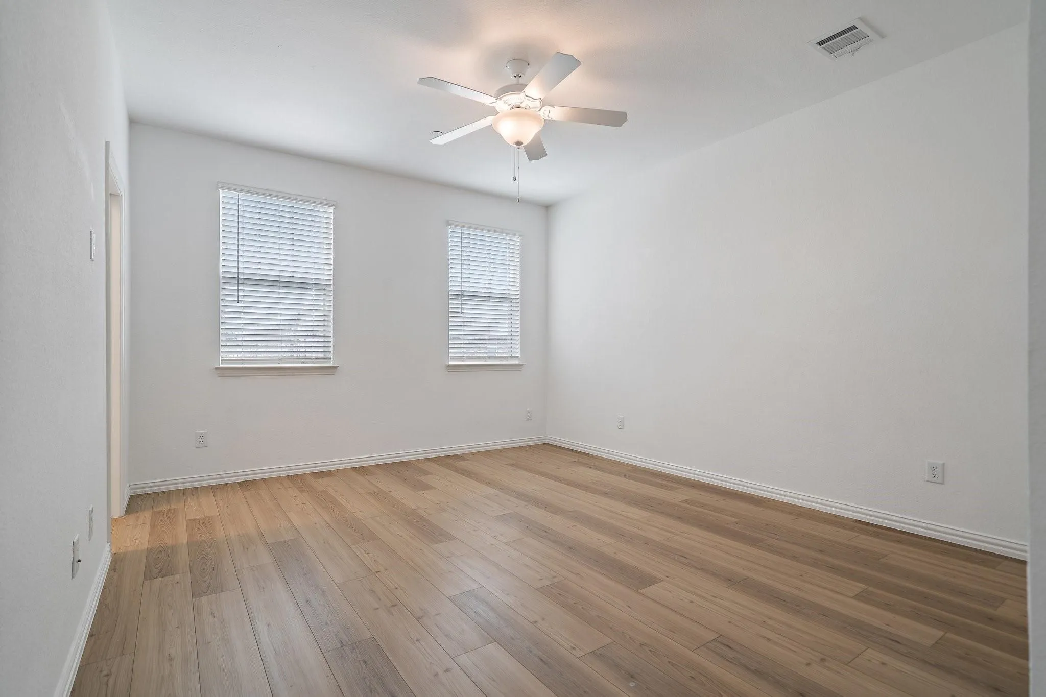 Room with wood-finish flooring, white walls, and a ceiling fan with integrated lighting