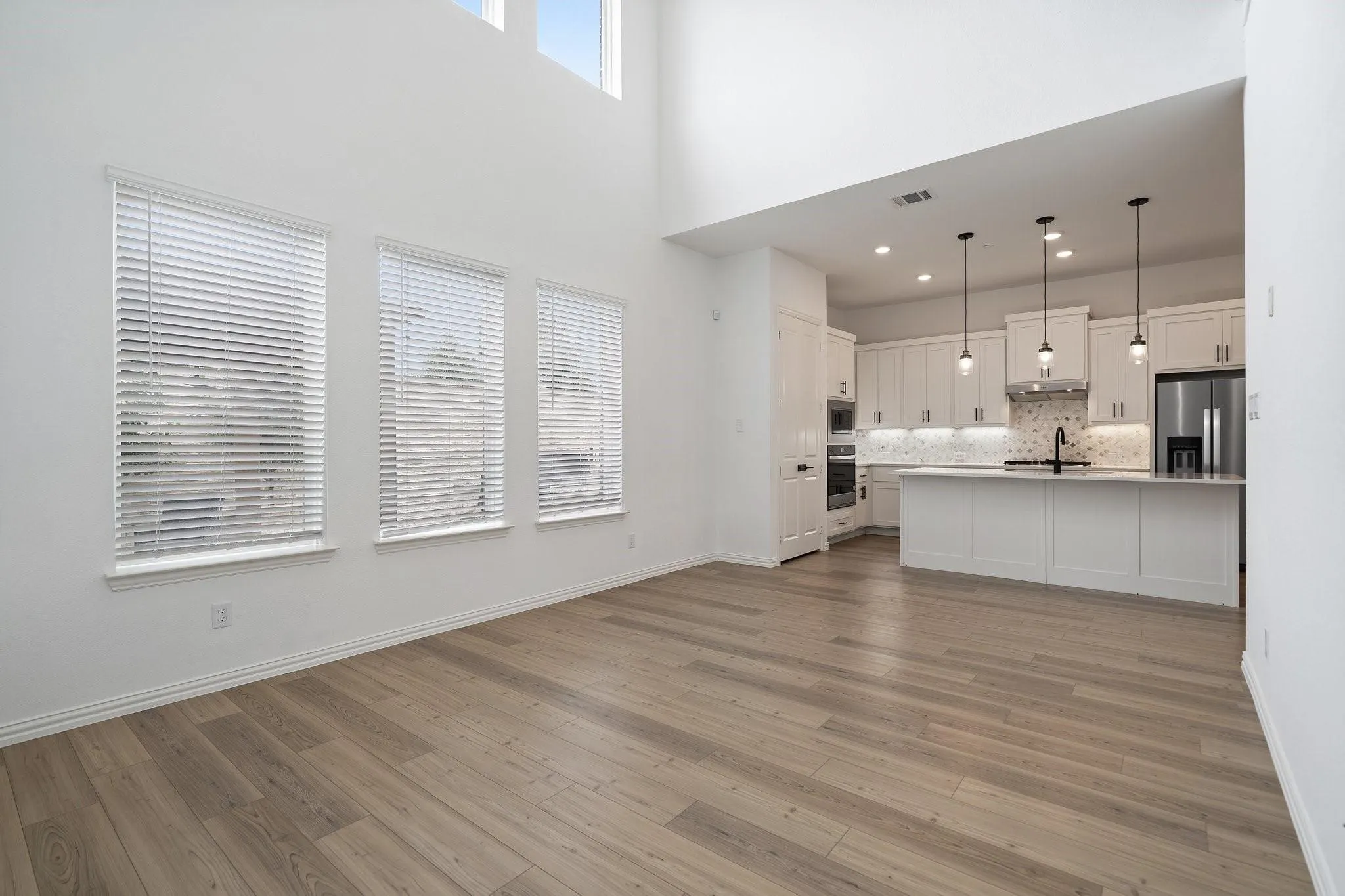 Open-concept living space featuring high ceilings, wood-finish flooring, and multiple windows