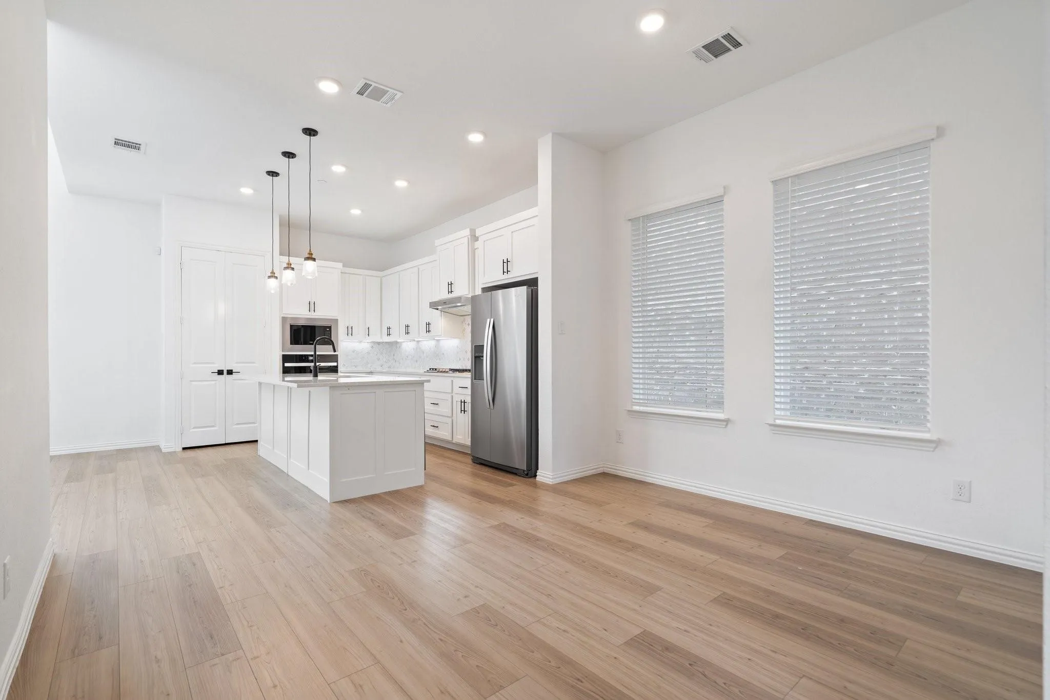 Open concept living space featuring wood-finish flooring, recessed lighting, and two large windows with blinds