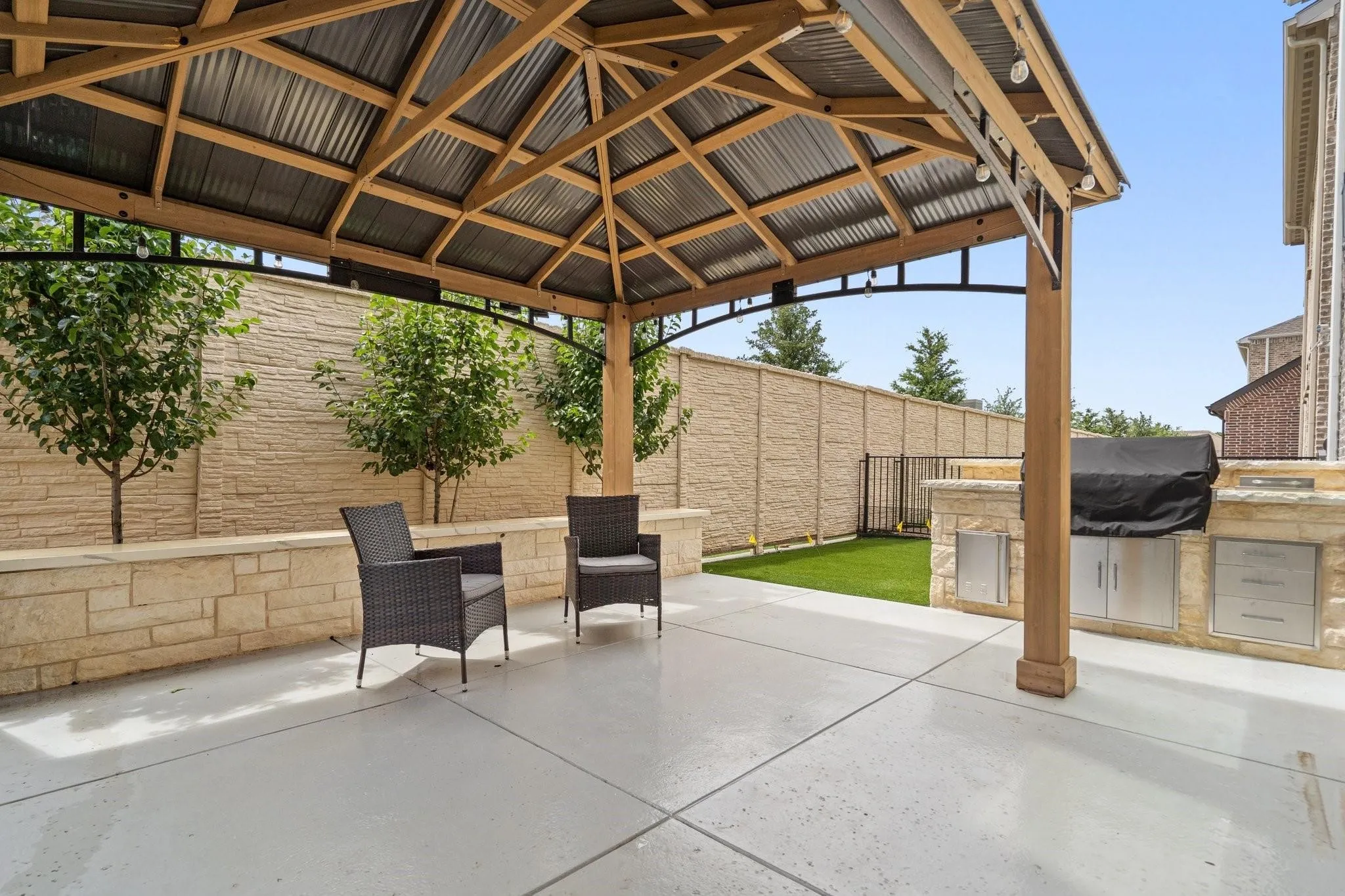 Expansive concrete patio featuring a wood gazebo with a metal roof and string lighting