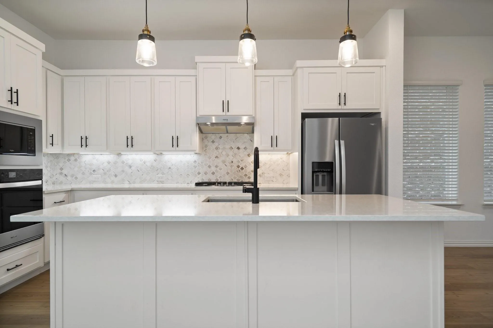 Kitchen featuring a large central island with light-toned countertops, white cabinetry with black hardware, stainless steel appliances, and a patterned tile backsplash