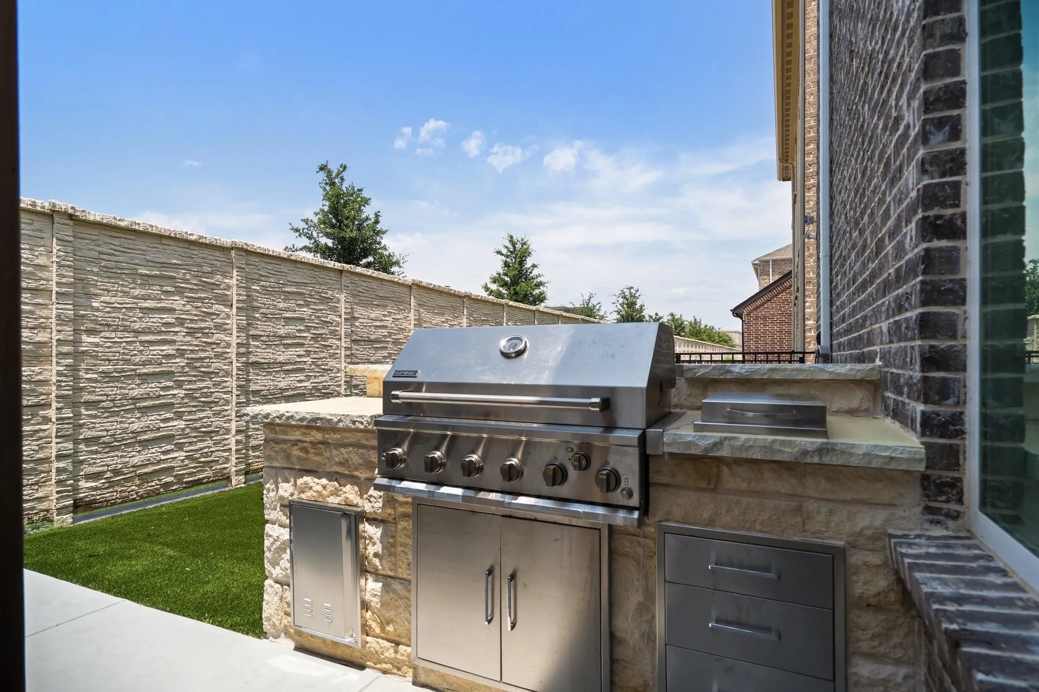 Outdoor kitchen featuring a built-in stainless steel grill, stone veneer base, stone countertops, and integrated stainless steel storage