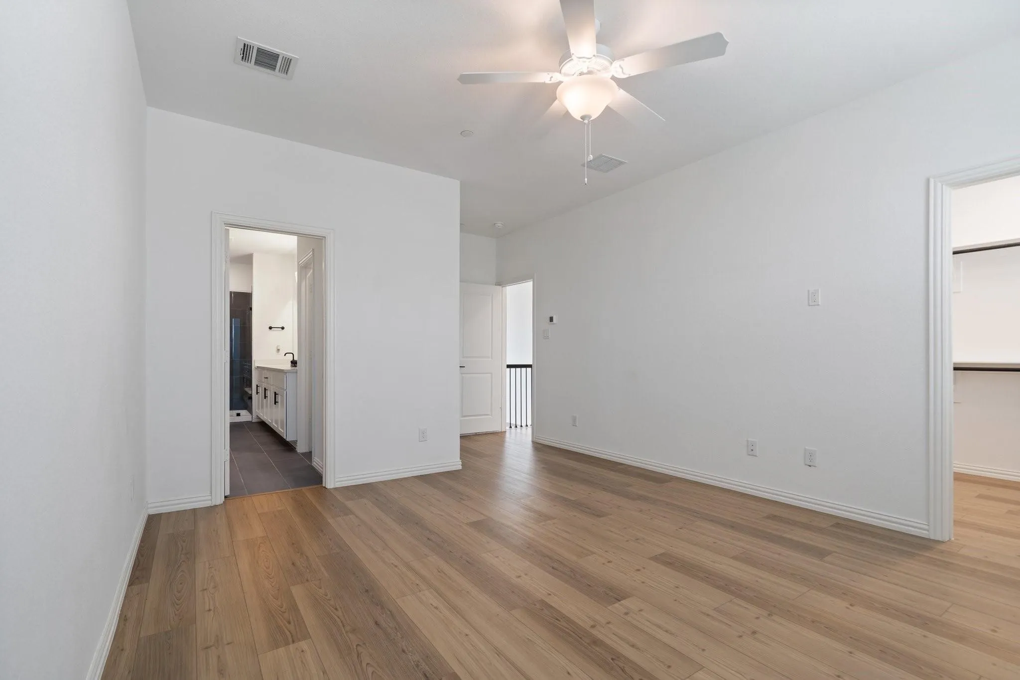 Spacious room featuring wood-finish flooring, crisp white walls, and a ceiling fan with integrated lighting