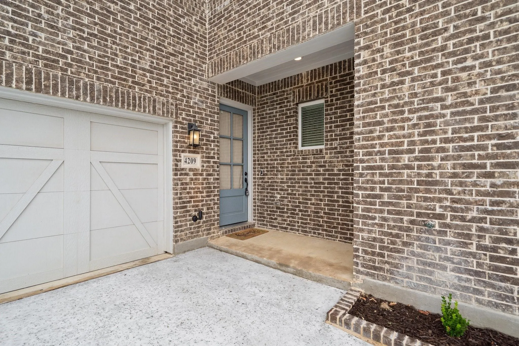 Brick exterior featuring a paneled garage door, a covered entryway with recessed lighting, an exterior wall sconce, and a front door with glass panels