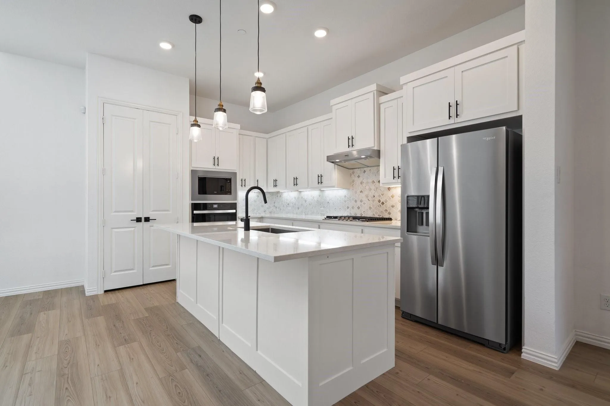 Contemporary kitchen featuring an island with a black gooseneck faucet, white shaker cabinetry, stainless steel appliances, and wood-finish flooring