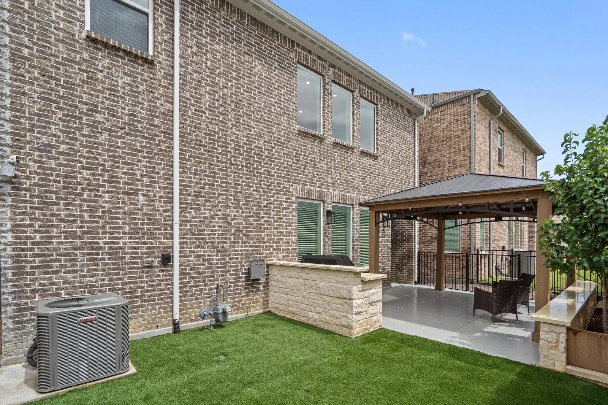 Private outdoor space featuring a covered patio with string lighting, an outdoor kitchen area with stone facing, a built-in planter box, and artificial turf