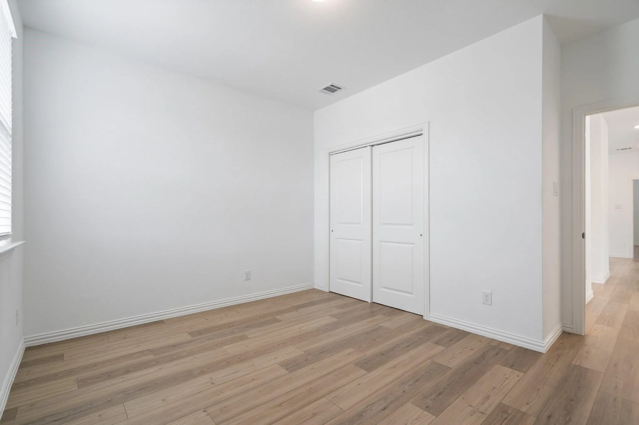 Room featuring wood-finish flooring, white walls, and a window with blinds