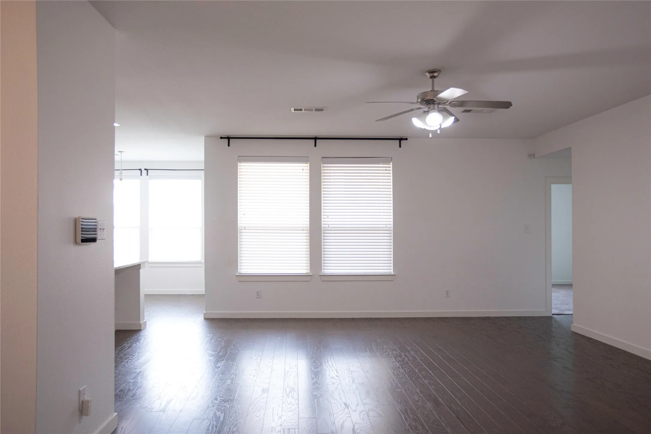 Spacious interior featuring dark wood-finish flooring, multiple windows with blinds, and a ceiling fan with integrated lighting