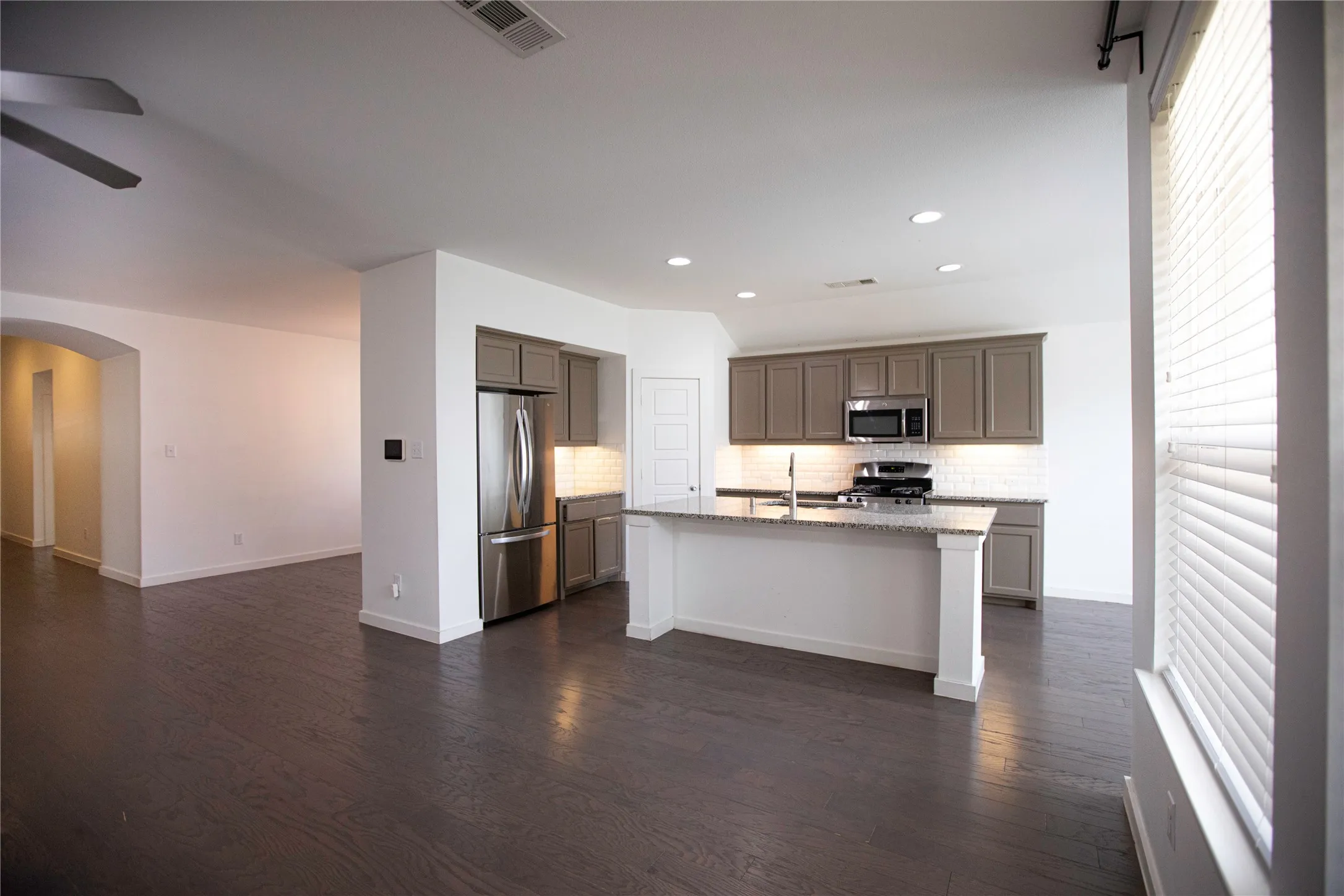 Open-concept kitchen with stainless steel appliances, granite countertops, an island with seating, and wood-finish flooring
