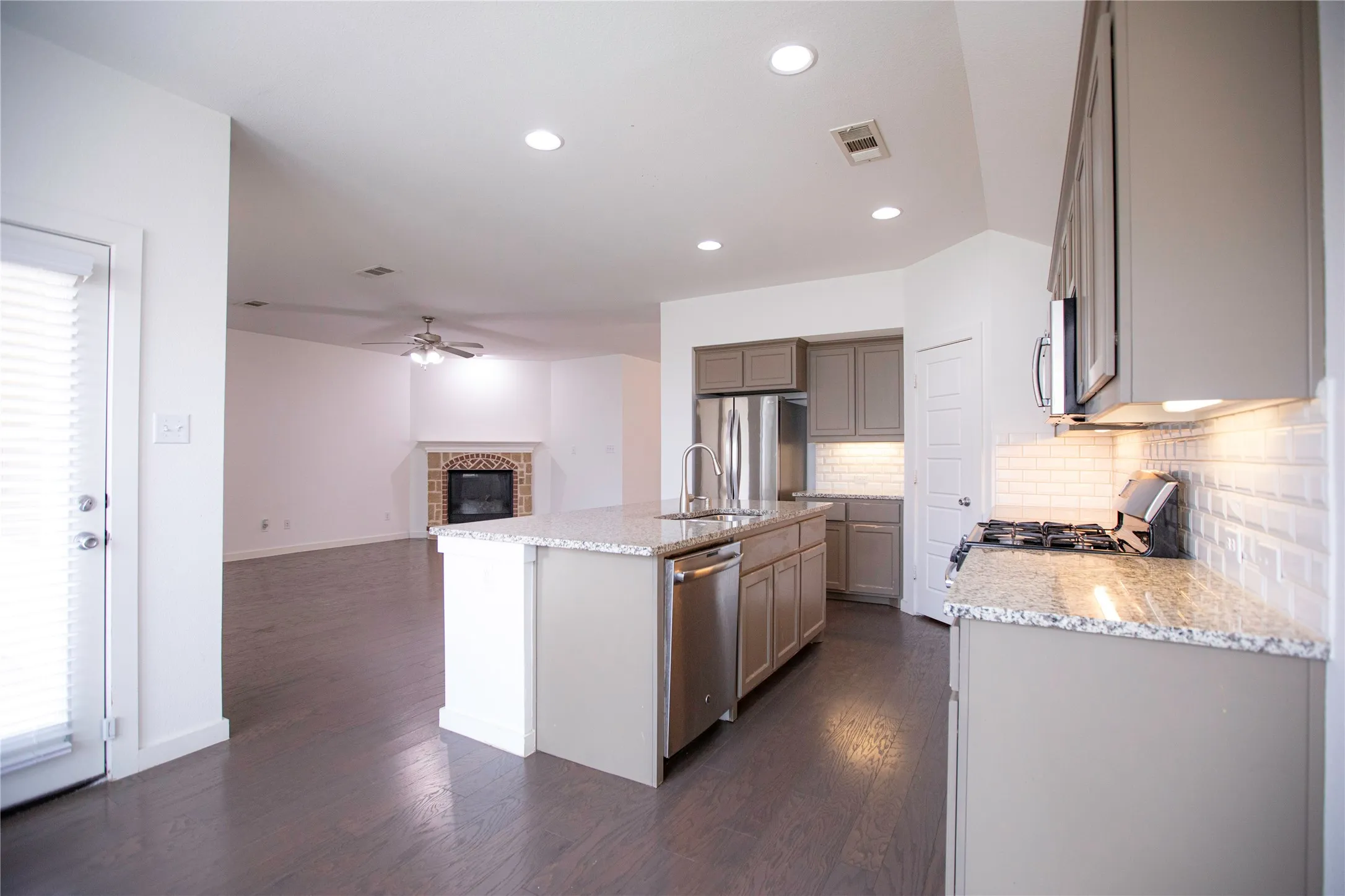 Kitchen featuring granite countertops, stainless steel appliances, a subway tile backsplash, recessed lighting, and wood-finish flooring