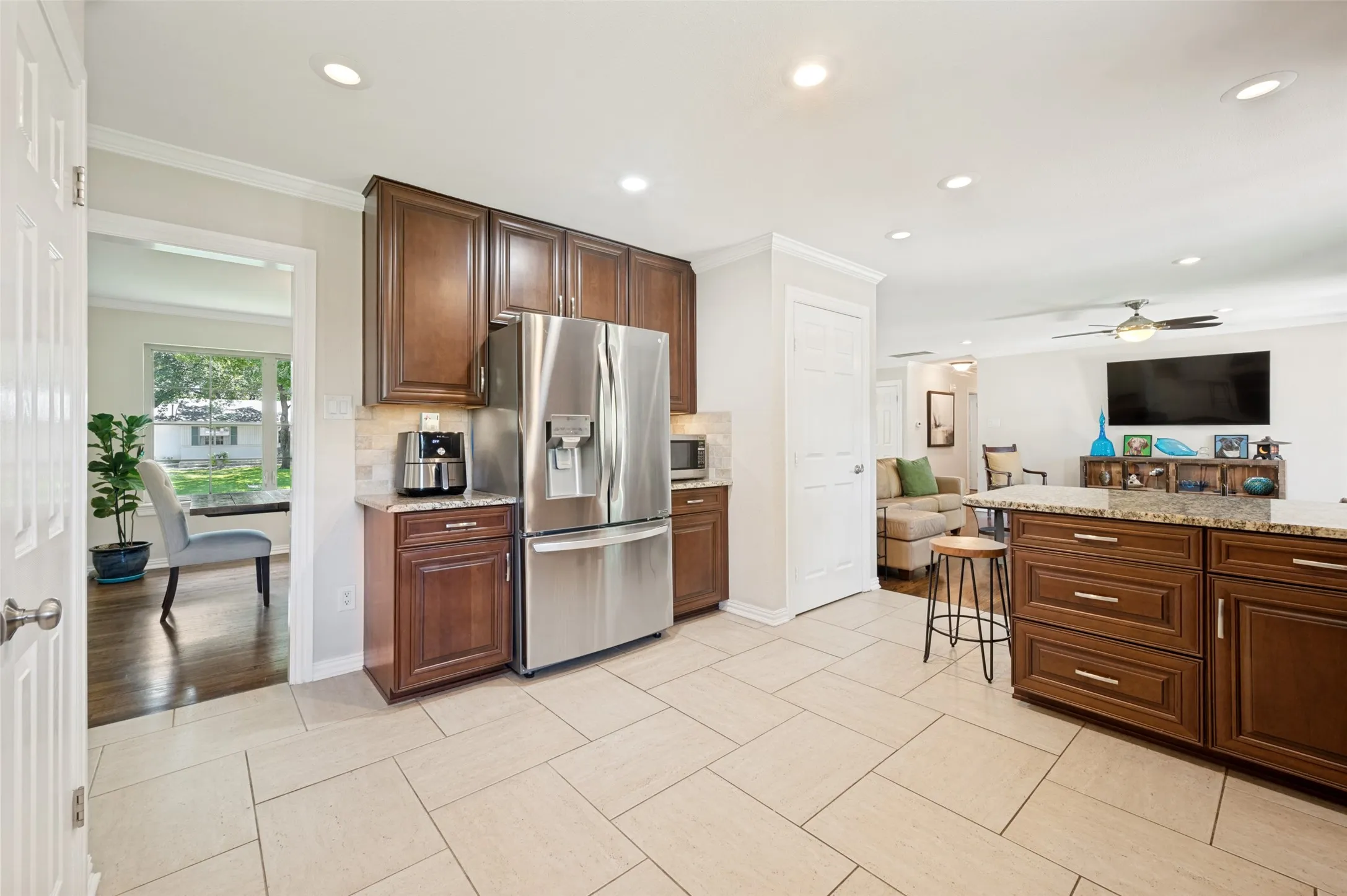 Kitchen featuring light-toned tile flooring, recessed lighting, wood cabinetry, stainless steel appliances, and a central island with a stone-finish countertop