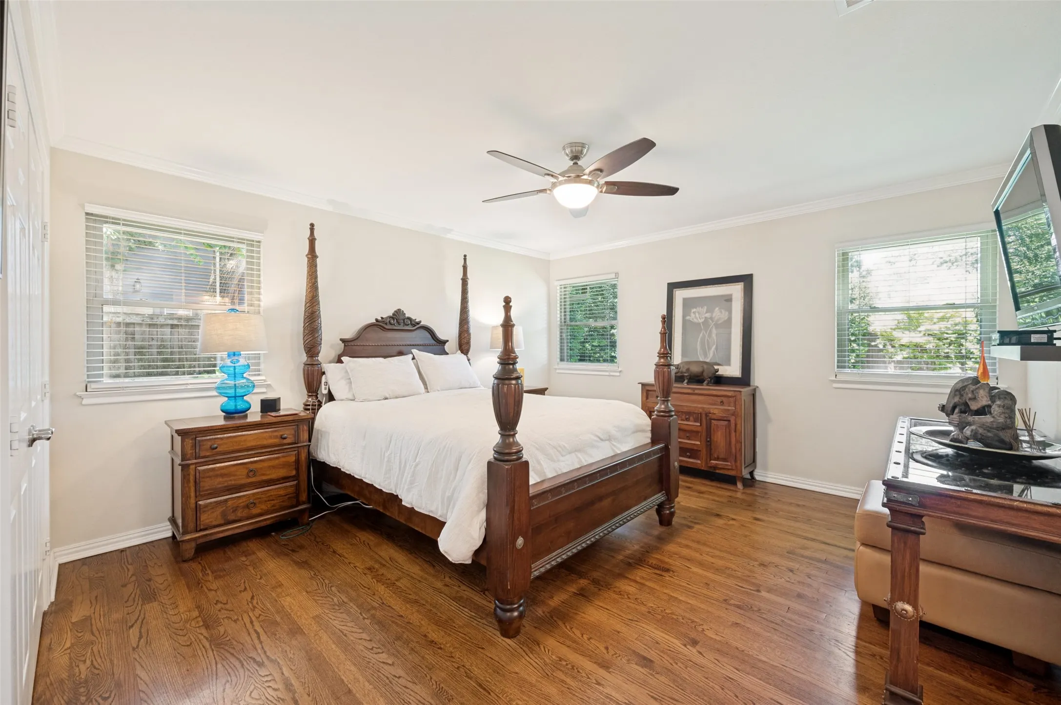 Spacious bedroom featuring wood-finish flooring, multiple windows with blinds, a ceiling fan with integrated lighting, and crown molding