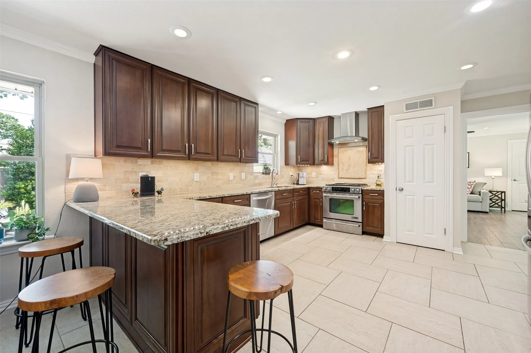 Kitchen featuring dark wood cabinetry, light-toned tile flooring, granite countertops, and stainless steel appliances