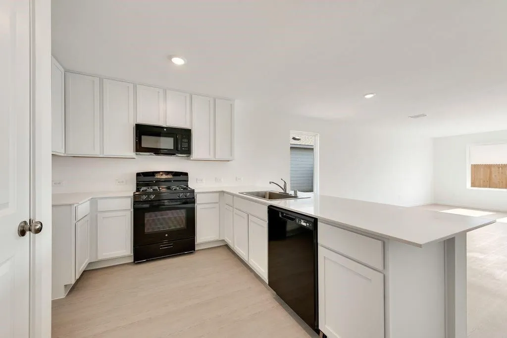 Kitchen featuring black appliances, a peninsula, light countertops, light wood-style flooring, and white cabinets