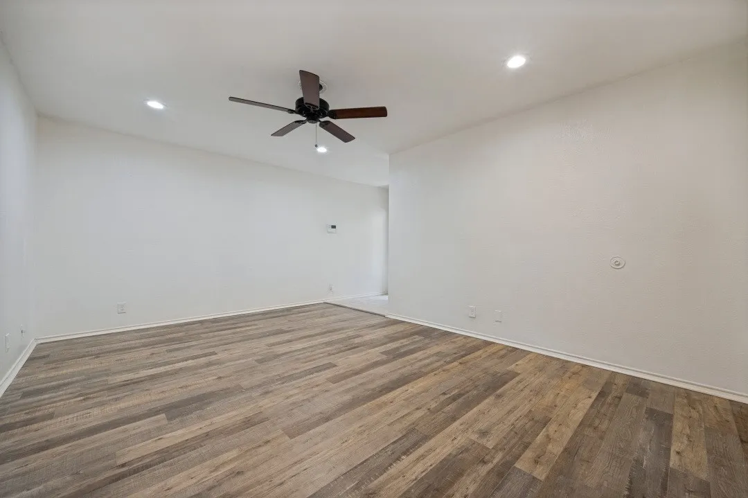 Spacious room featuring wood-finish flooring, recessed lighting, a ceiling fan with dark wood-finish blades, white baseboards, and neutral wall tones