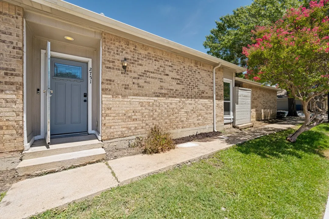 Brick exterior featuring a gray paneled door with decorative glass insert, concrete walkway, and a vibrant flowering tree
