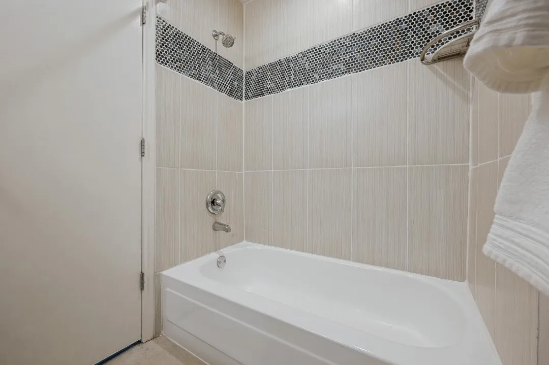 Bathtub with a chrome showerhead and faucet, surrounded by light-toned rectangular wall tiles