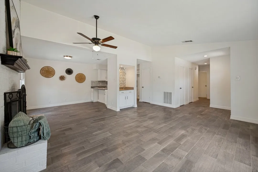 Spacious living area featuring wood-finish tile flooring, a white brick fireplace with a dark wood mantel, and a ceiling fan