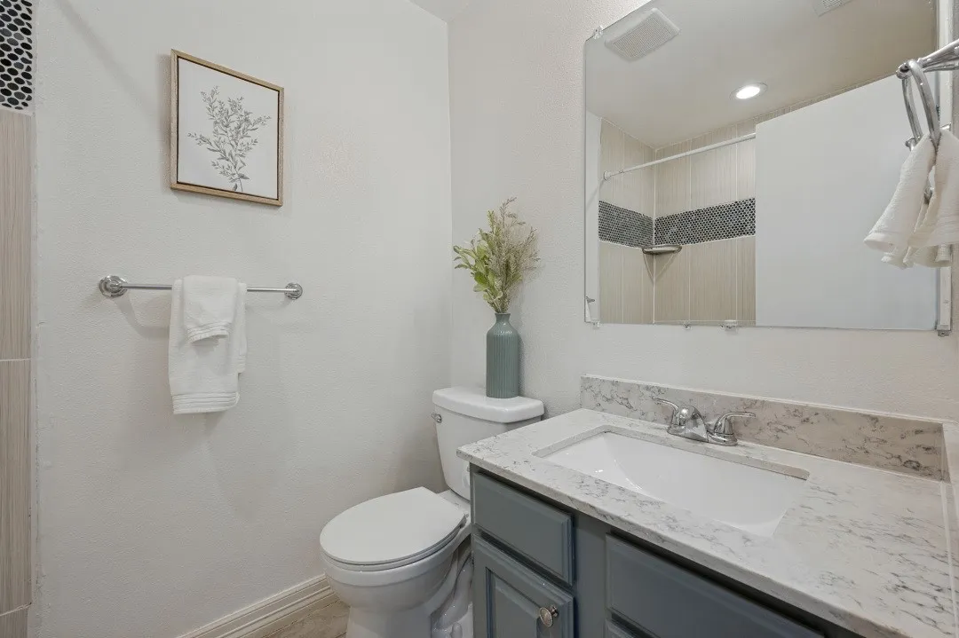Bathroom featuring a vanity with an integrated sink and light-toned countertop, a mounted mirror, and a shower with tiled walls
