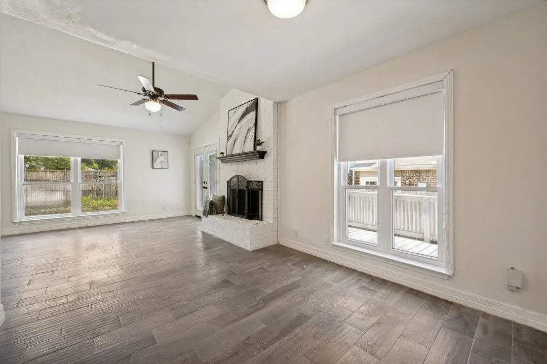 Living area featuring vaulted ceilings, wood-finish flooring, and a white brick fireplace with a dark mantel