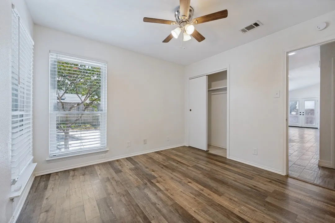 Room featuring wood-finish flooring, a ceiling fan with light kit, and a double-pane window with white blinds