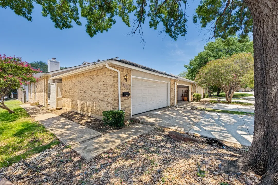 Brick exterior featuring an attached garage with a white door, concrete driveway, and a paved walkway