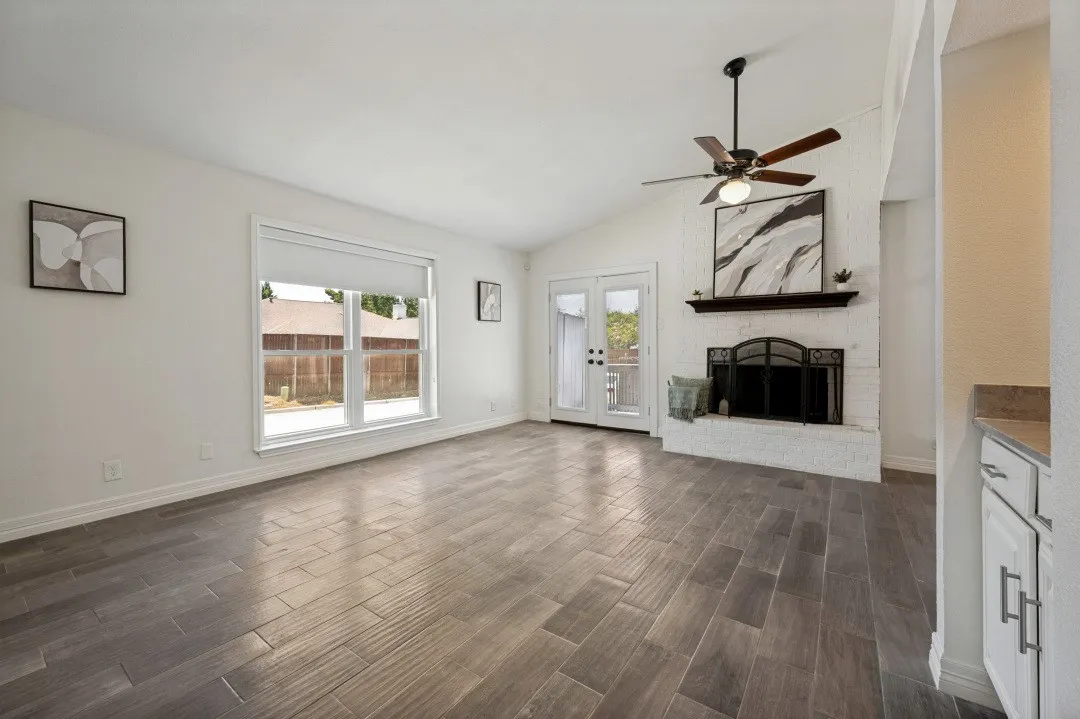 Living area featuring wood-finish tile flooring, a white brick fireplace with a wood mantle, and a vaulted ceiling with a fan