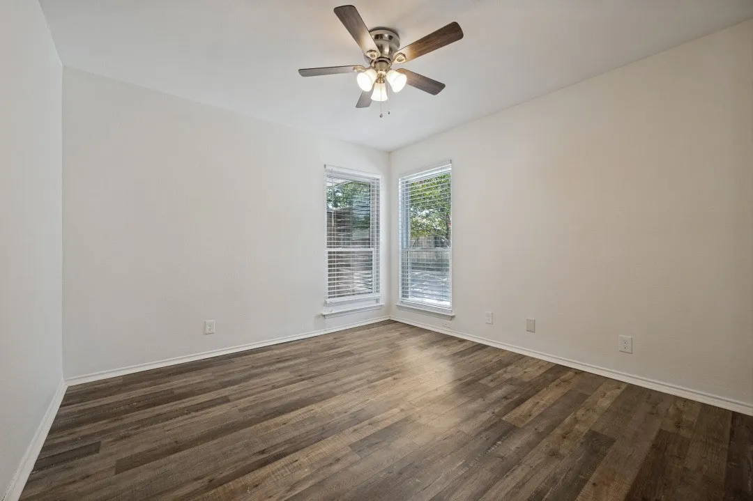 Room featuring wood-finish flooring, two large windows with blinds, a ceiling fan with integrated lighting, white walls, and white trim