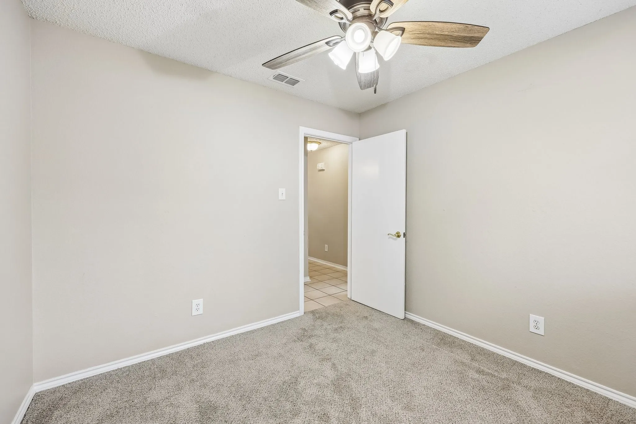 Carpeted room featuring a ceiling fan with light fixture, neutral wall finishes, white trim, and a white interior door