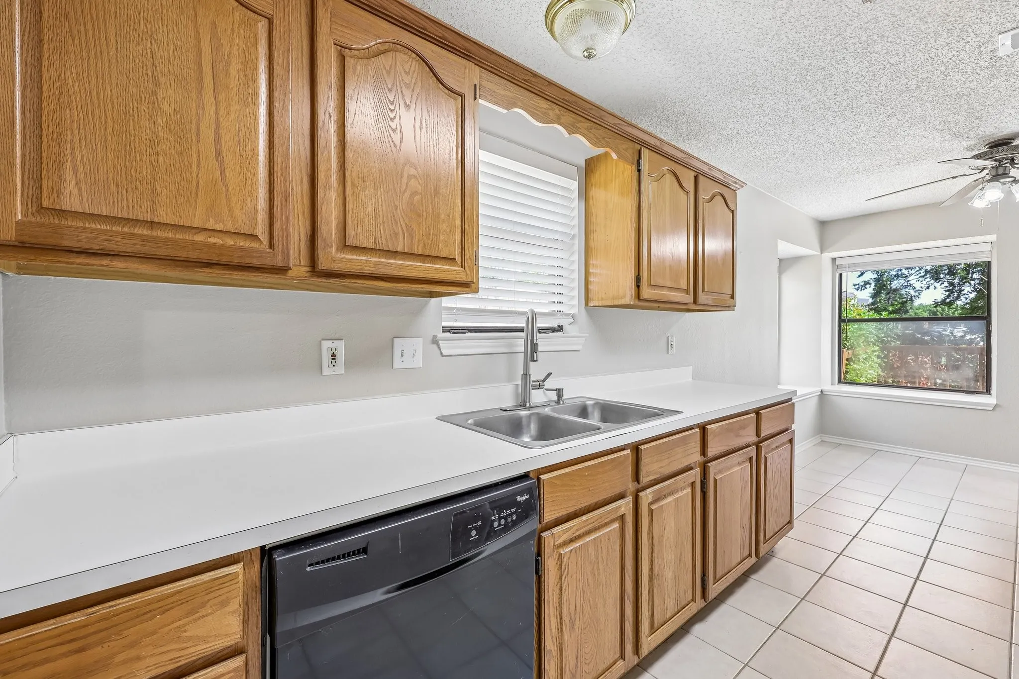 Kitchen featuring wood cabinetry, white countertops, dual basin stainless steel sink with a gooseneck faucet, black dishwasher, and tile flooring