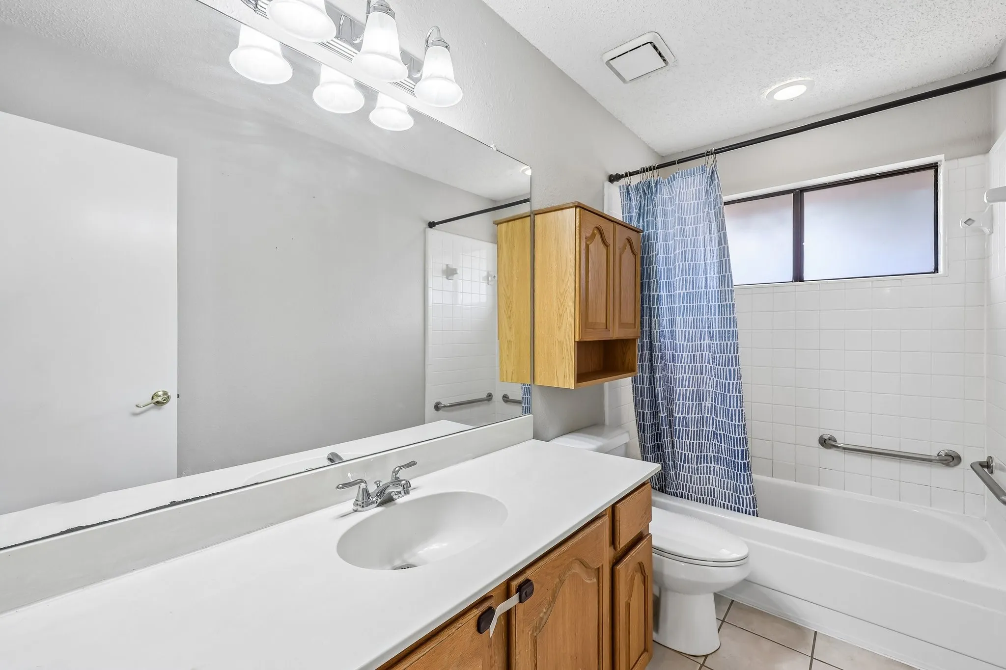 Bathroom featuring a vanity with a white countertop, wood-finish cabinetry, a built-in tub with white subway tile surround, and a frosted window