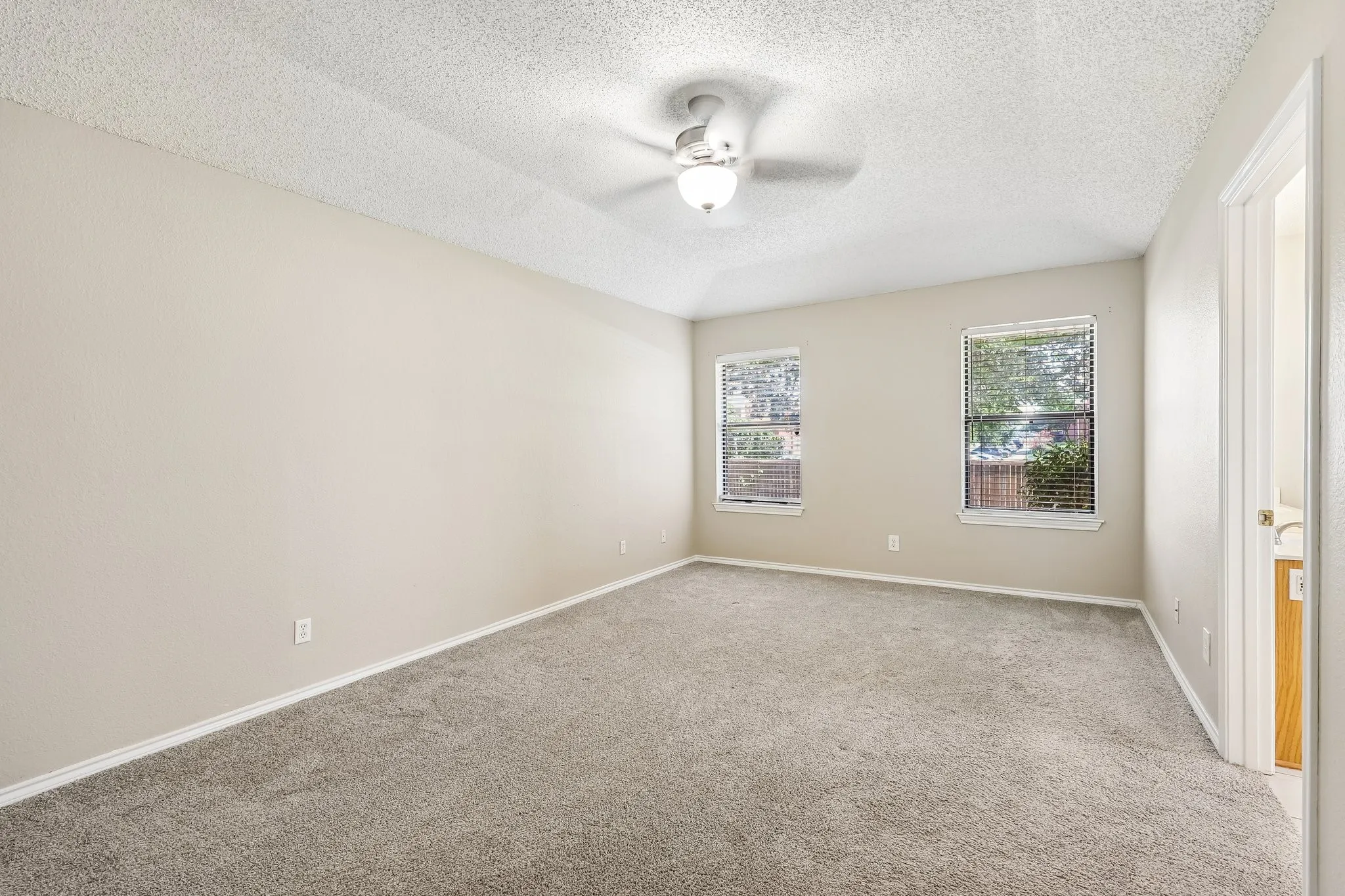 Expansive room featuring neutral-toned walls, gray carpeting, and a ceiling fan with integrated lighting