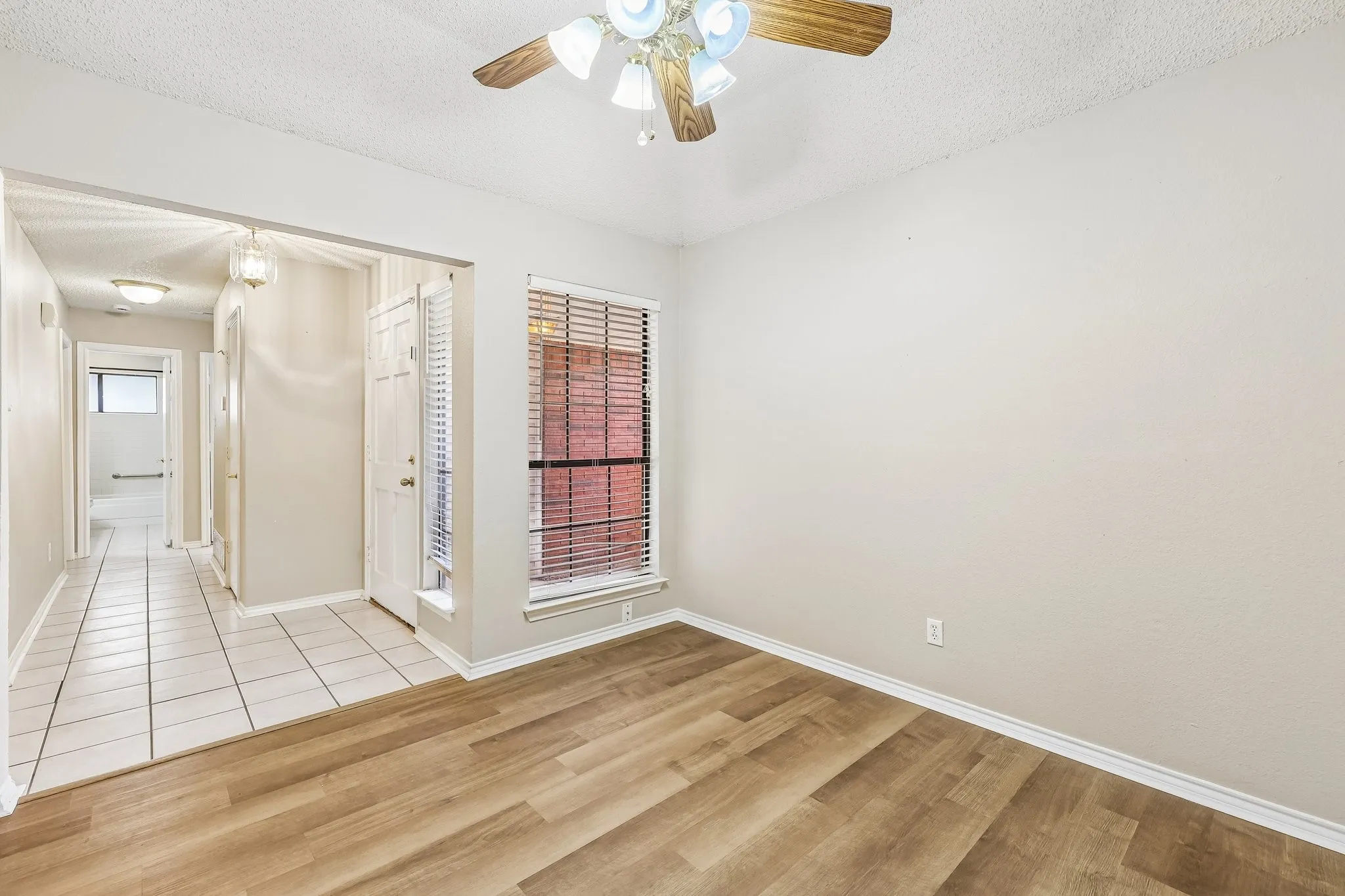 Spacious room featuring wood-finish flooring, neutral wall paint, and a ceiling fan with light fixture