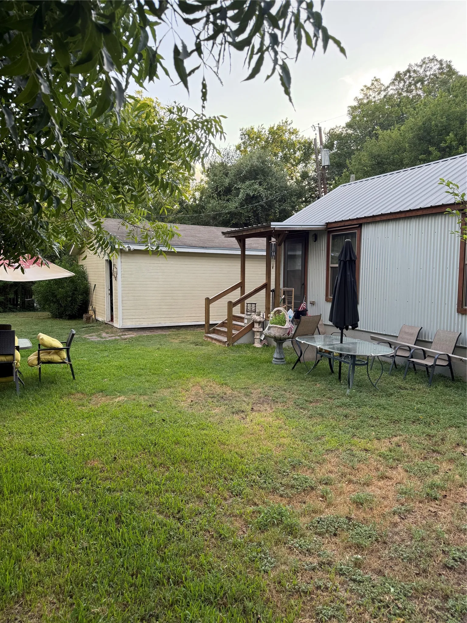 Expansive green space featuring a detached building with an overhead door, a covered porch, and a main structure with a metal roof