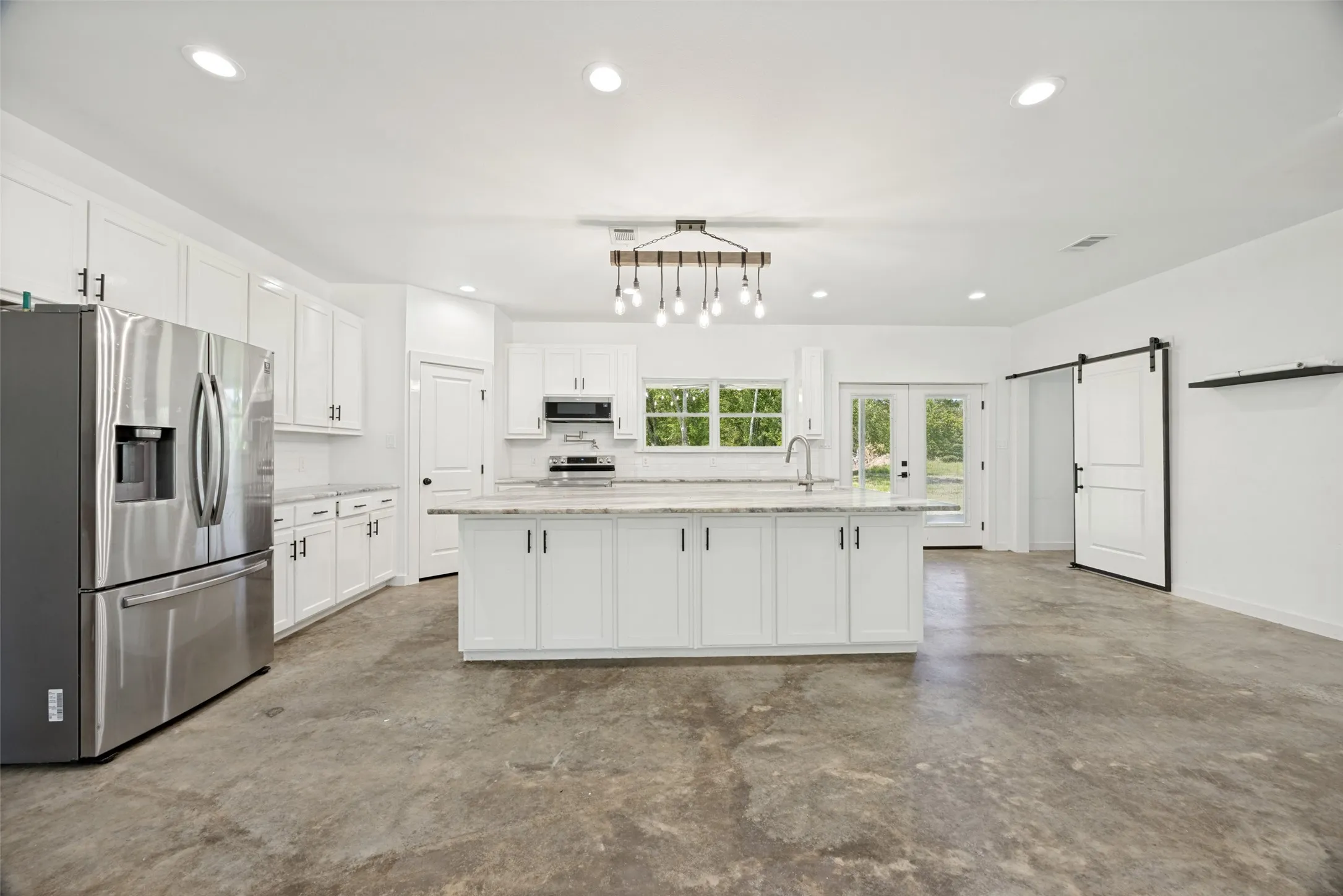 Open-concept kitchen featuring an expansive center island, white cabinetry, integrated stainless steel appliances, and concrete-finish flooring