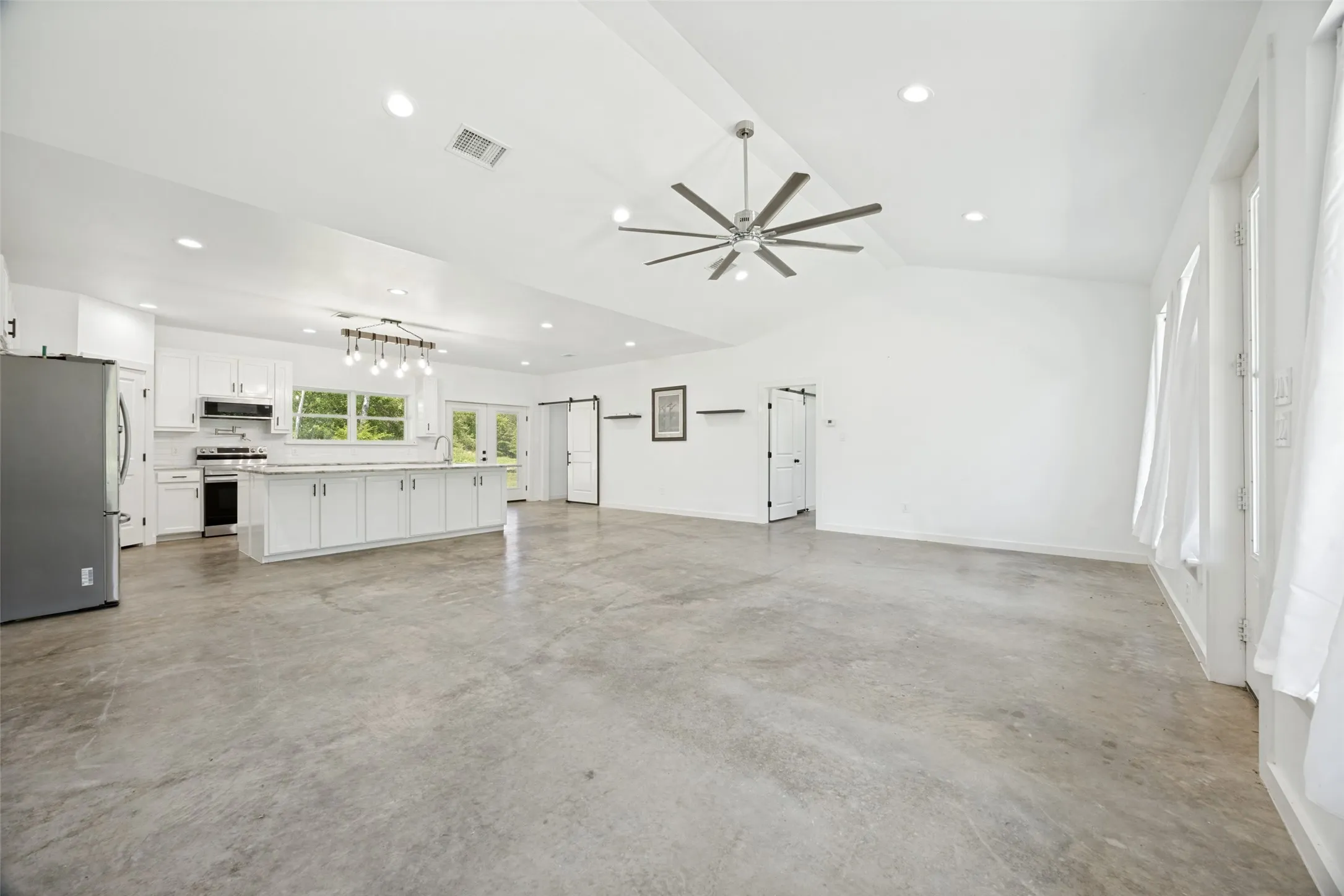 Spacious open-concept interior featuring concrete flooring, a vaulted ceiling, and recessed lighting