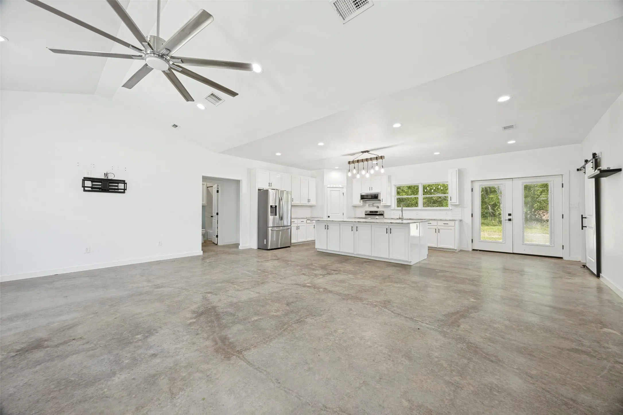 Open-concept living space featuring vaulted ceilings, polished concrete flooring, recessed lighting, and a modern ceiling fan