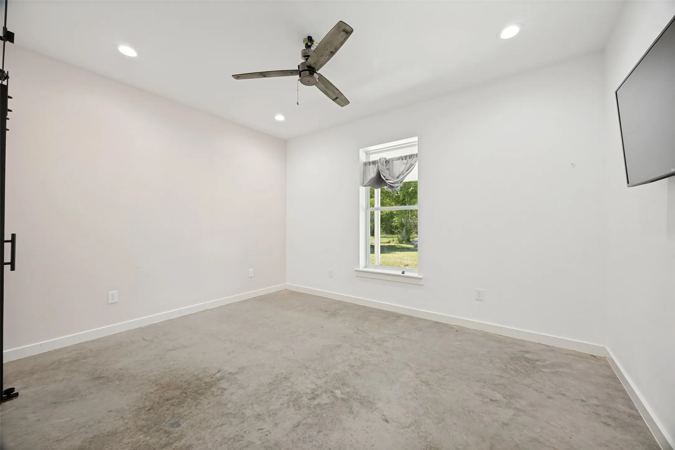 Interior room featuring a ceiling fan, recessed lighting, concrete flooring, and a single window with outdoor scenery