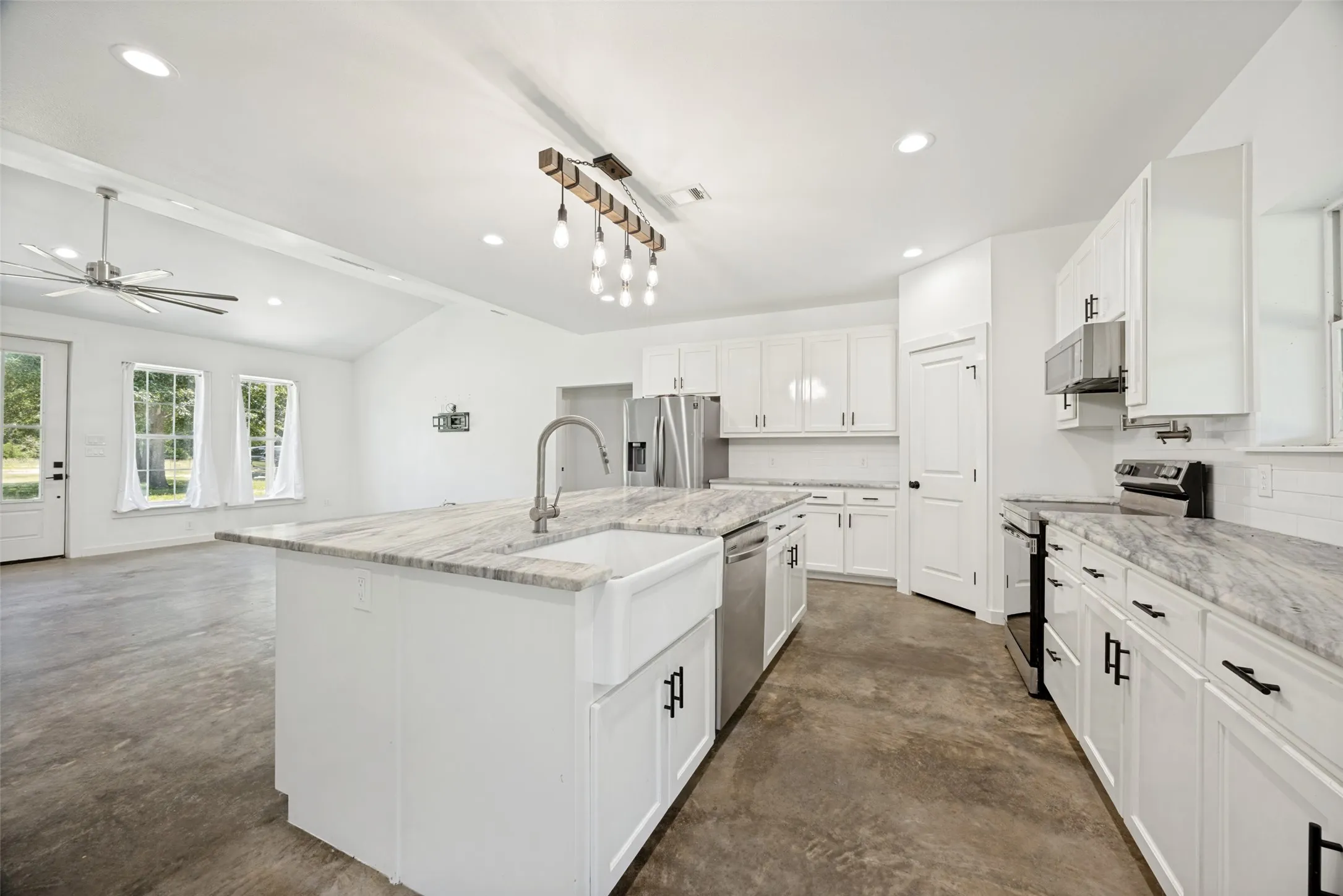 Kitchen featuring a large island with an apron-front sink and high-arc faucet, white cabinetry, stainless steel appliances, and light-toned countertops