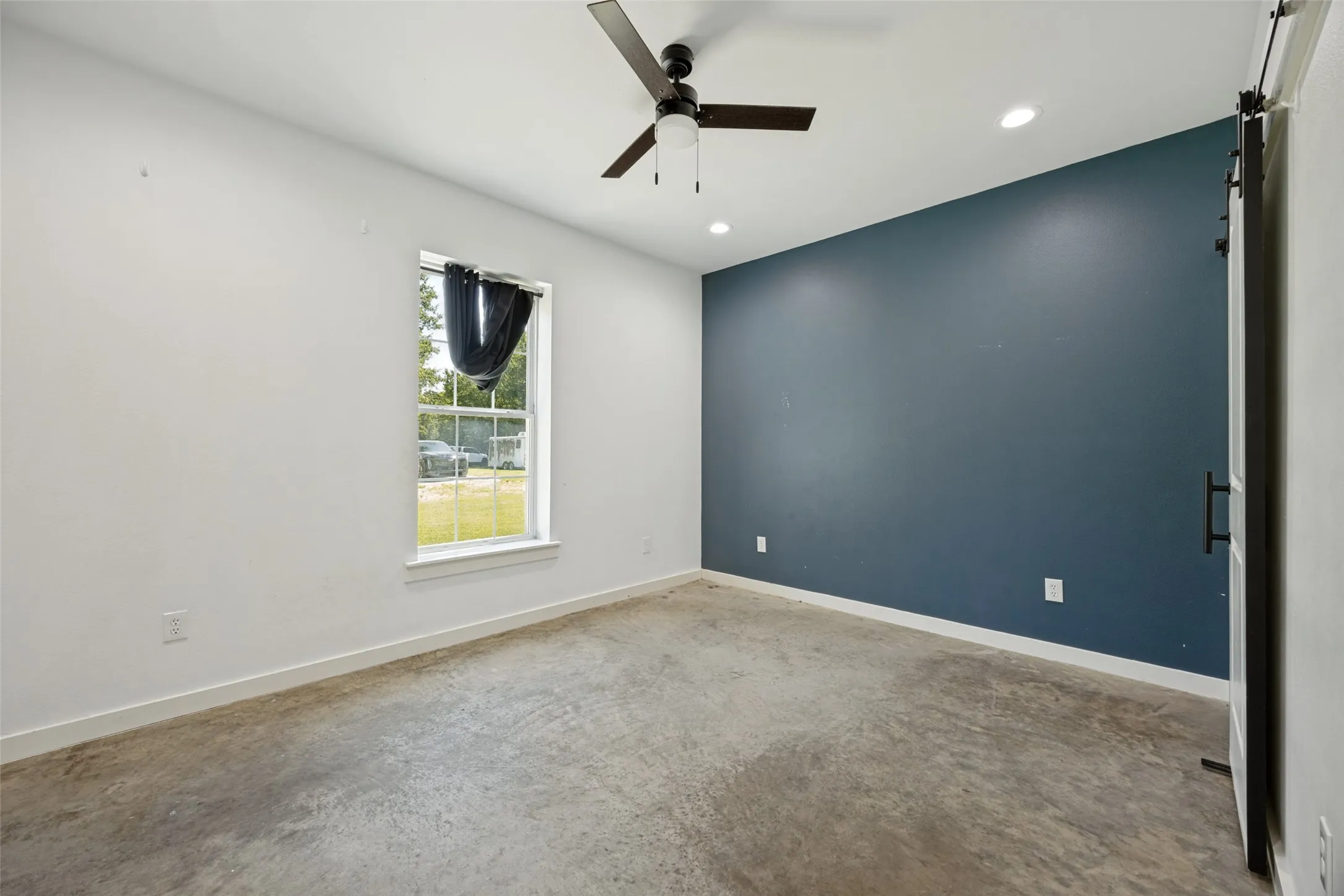Interior room featuring a bold accent wall, concrete flooring, a ceiling fan, recessed lighting, and a single window