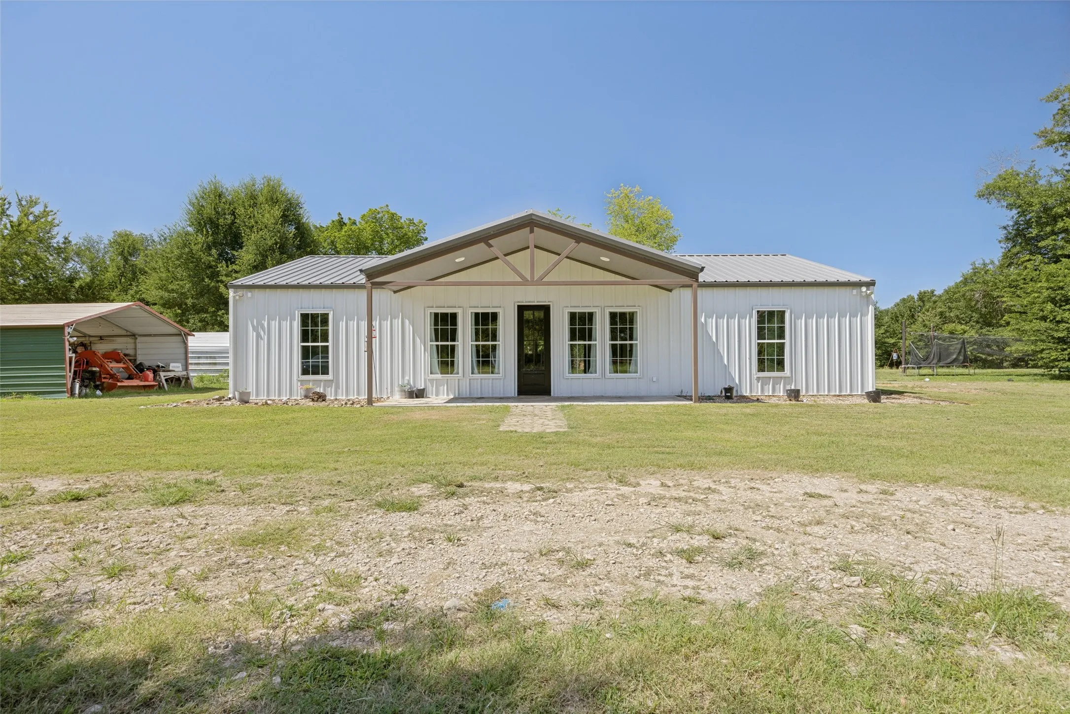 White metal siding structure with a covered entry, multiple windows, and a black front door