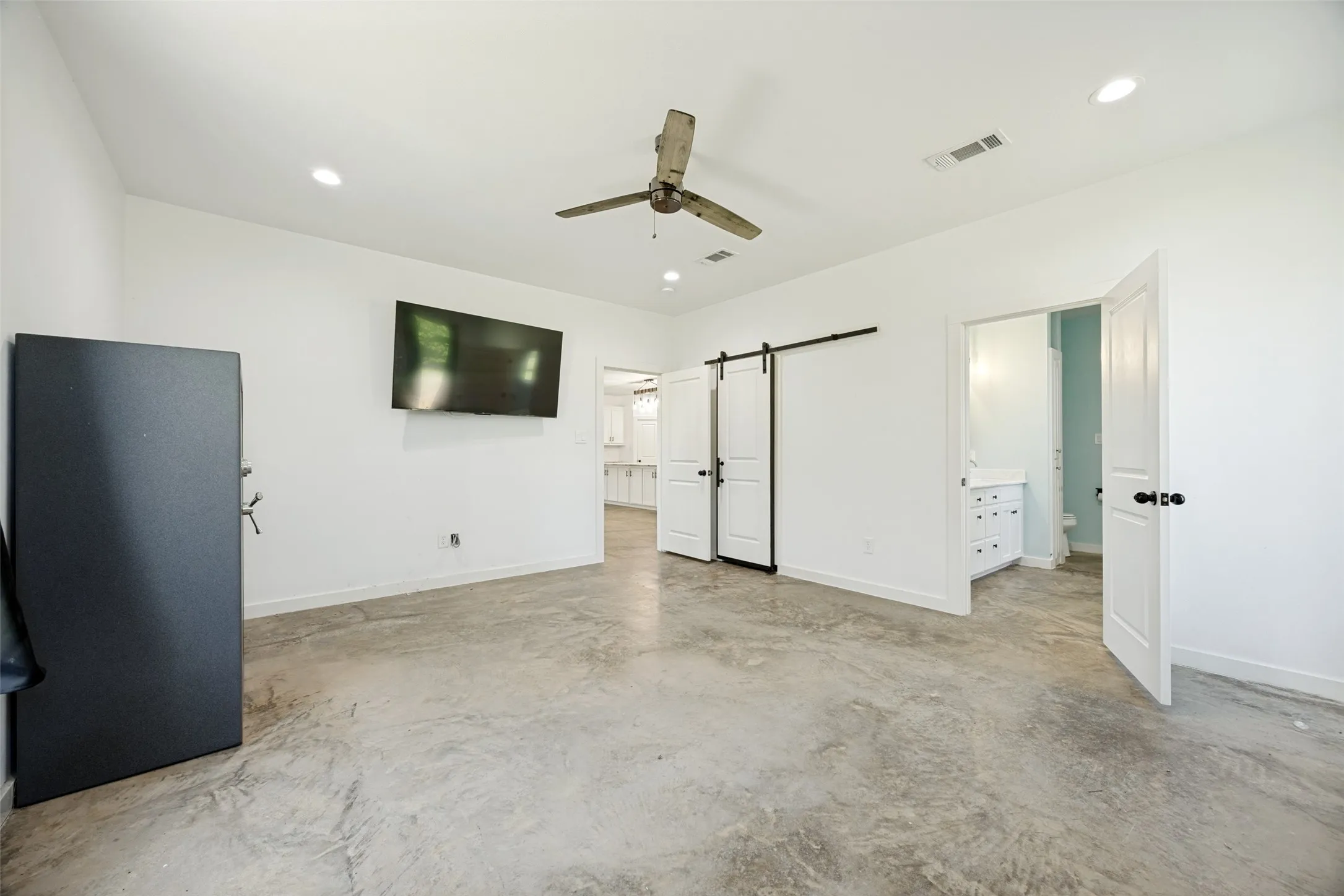 Spacious room featuring concrete flooring, a ceiling fan with integrated lighting, recessed lighting, and a white barn door entry