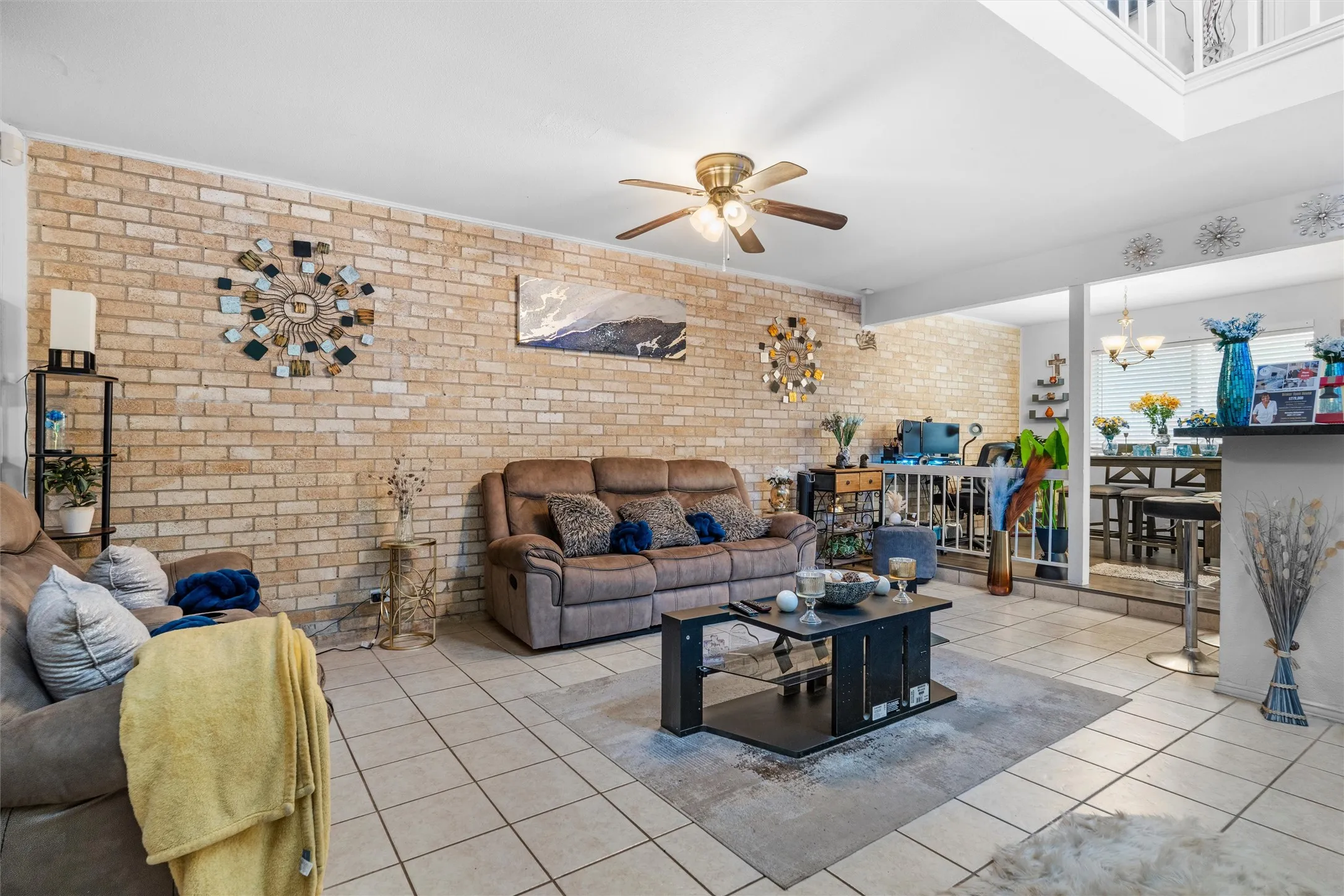 Exposed brick accent wall, tile flooring, ceiling fan, and open-concept design with a breakfast bar