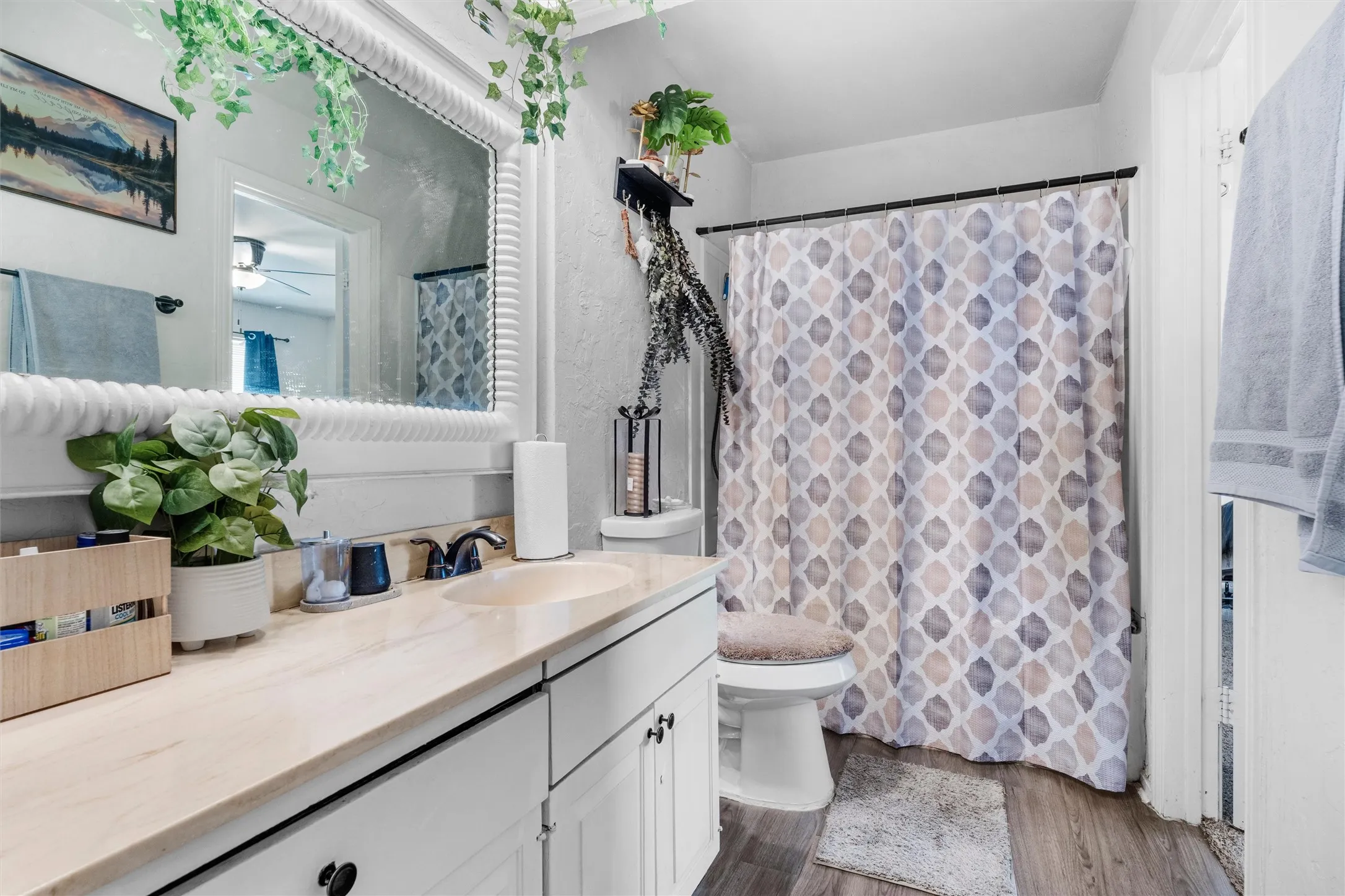 White vanity with a single basin and black faucet, framed mirror, and wood-finish flooring