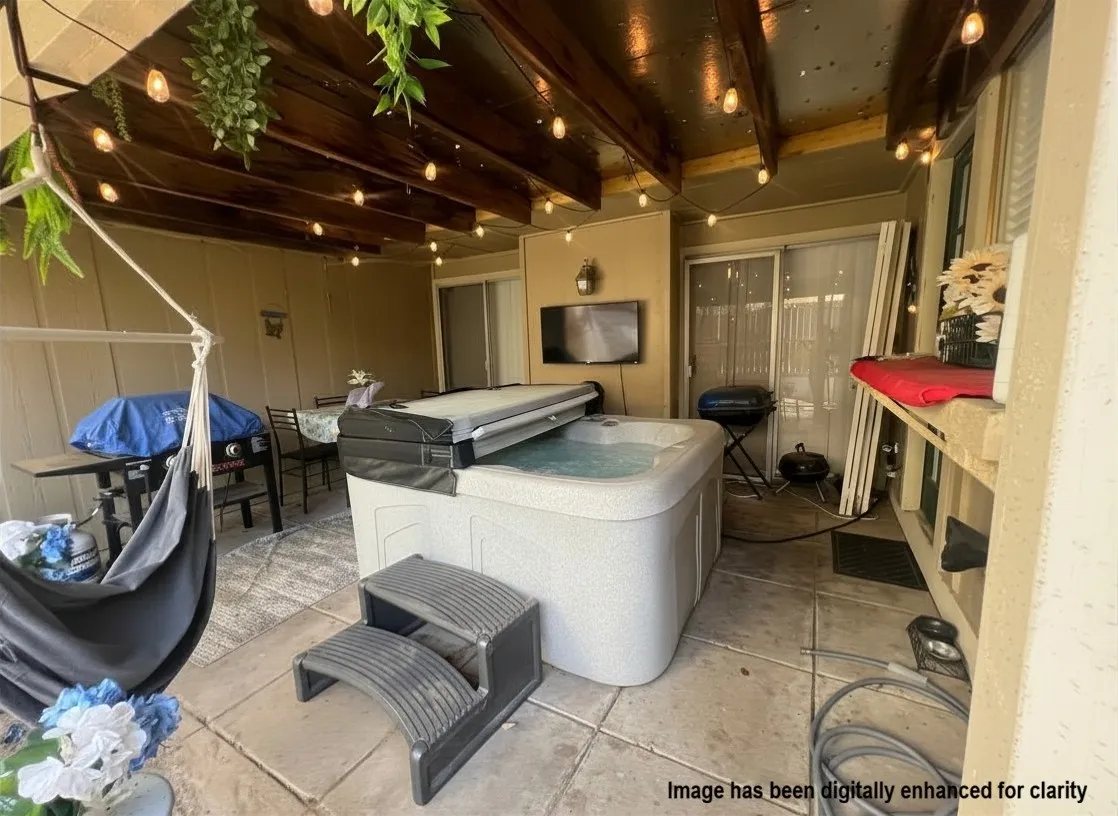Covered patio featuring an inset hot tub with steps, string lighting, and a wood-beamed ceiling