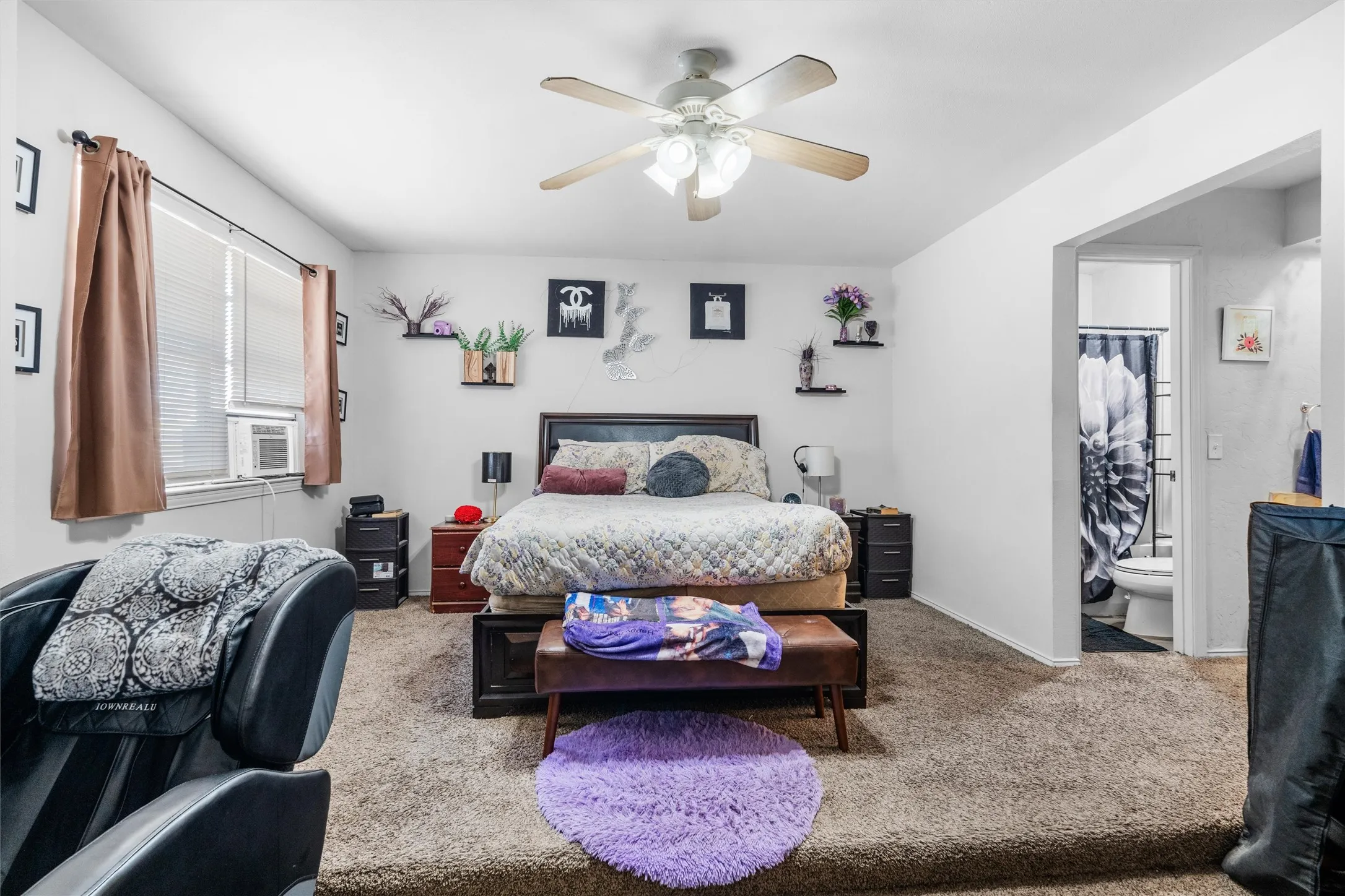 Spacious primary bedroom with carpeted flooring, ceiling fan with integrated lighting, and abundant natural light from large window with custom window treatments