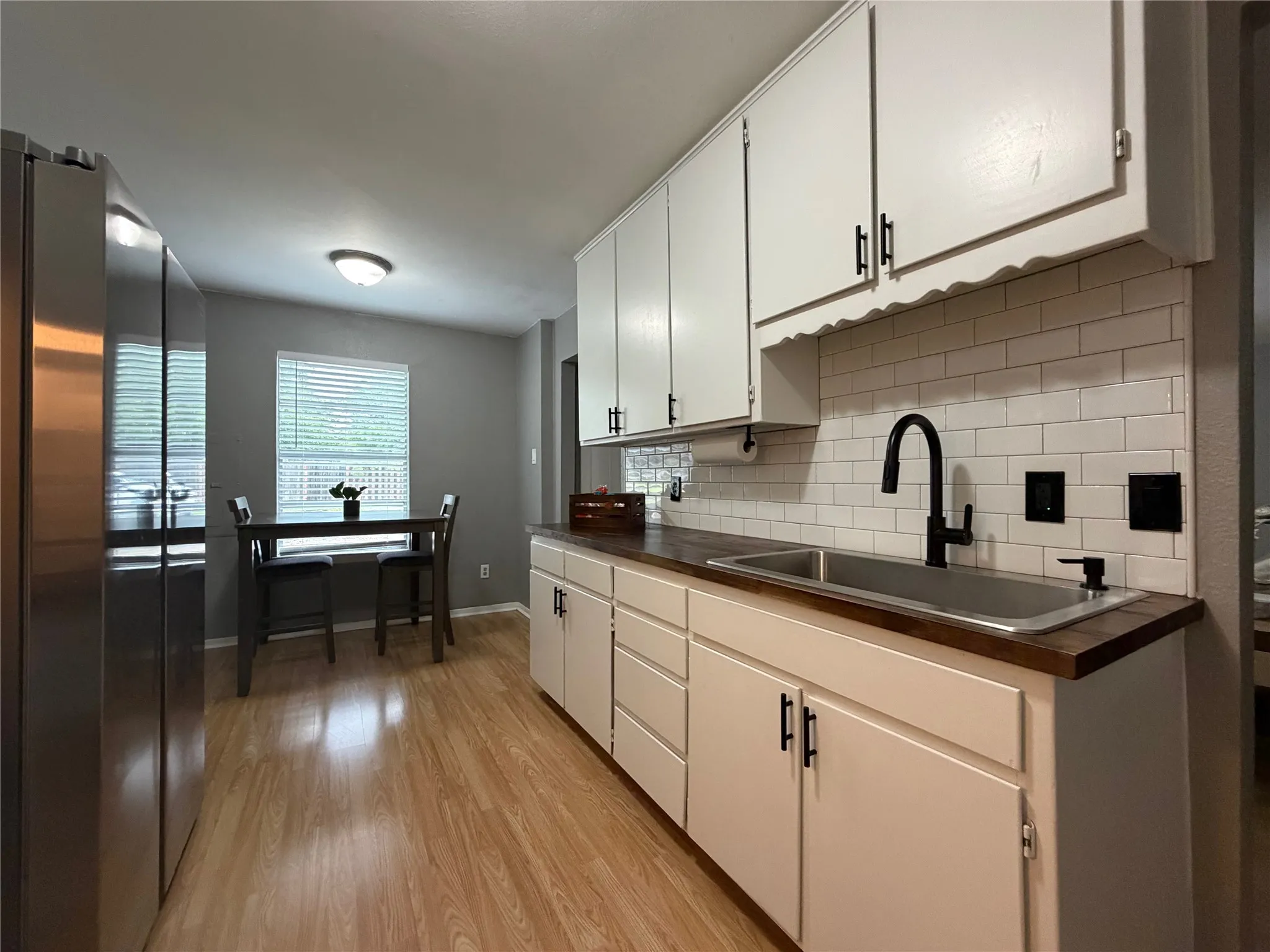 Kitchen featuring wood-finish flooring, white cabinetry with matte black hardware, subway tile backsplash, and a stainless steel sink with a matte black faucet