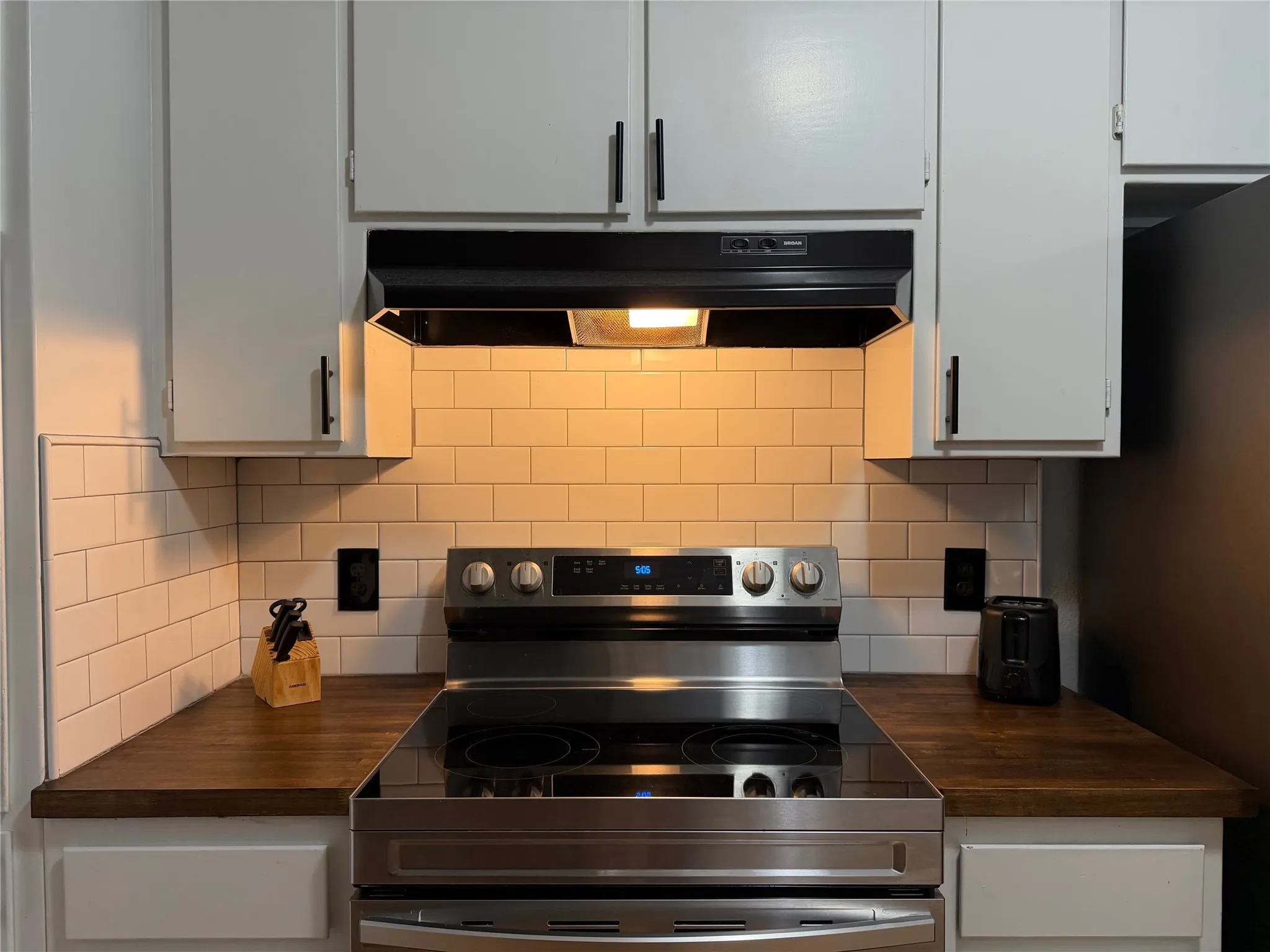 Kitchen featuring a stainless steel electric range, white subway tile backsplash, and wood-finish countertops