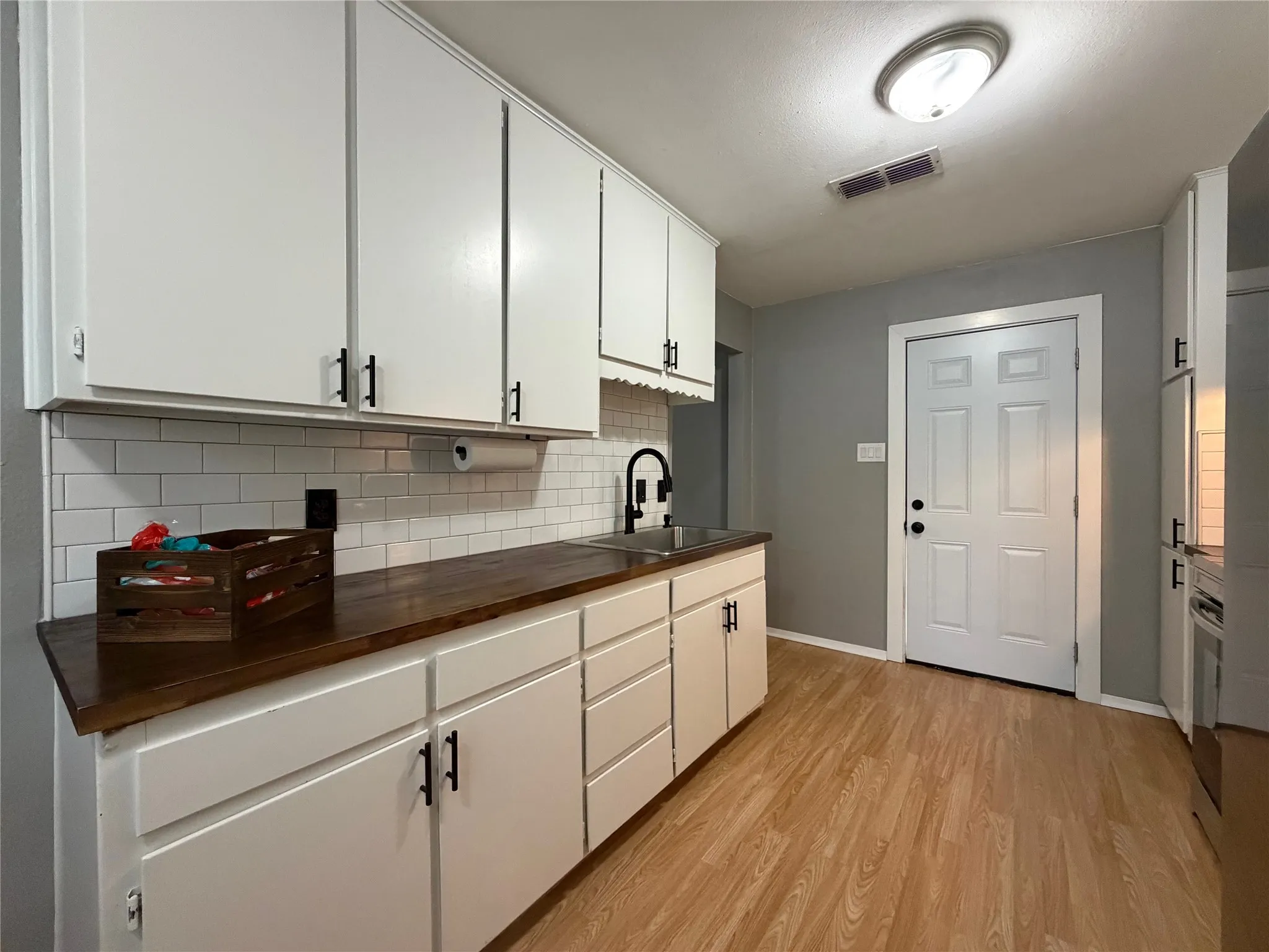 Kitchen featuring white cabinetry with matte black hardware, wood-finish countertops, subway tile backsplash, and light wood-look flooring